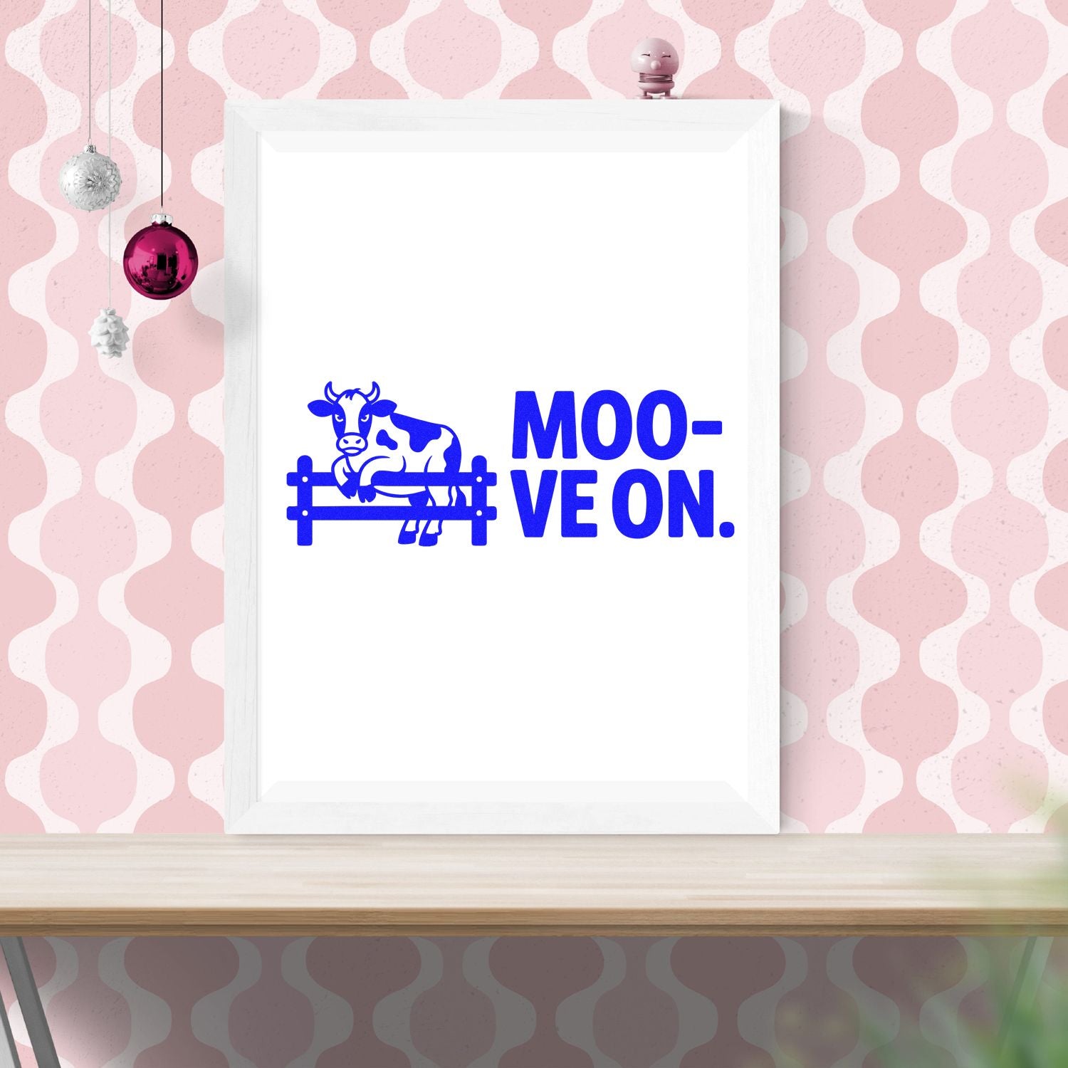 Blue cow stamp and seal design reading MOO-VEON. on a white framed print, against a pink patterned wall.