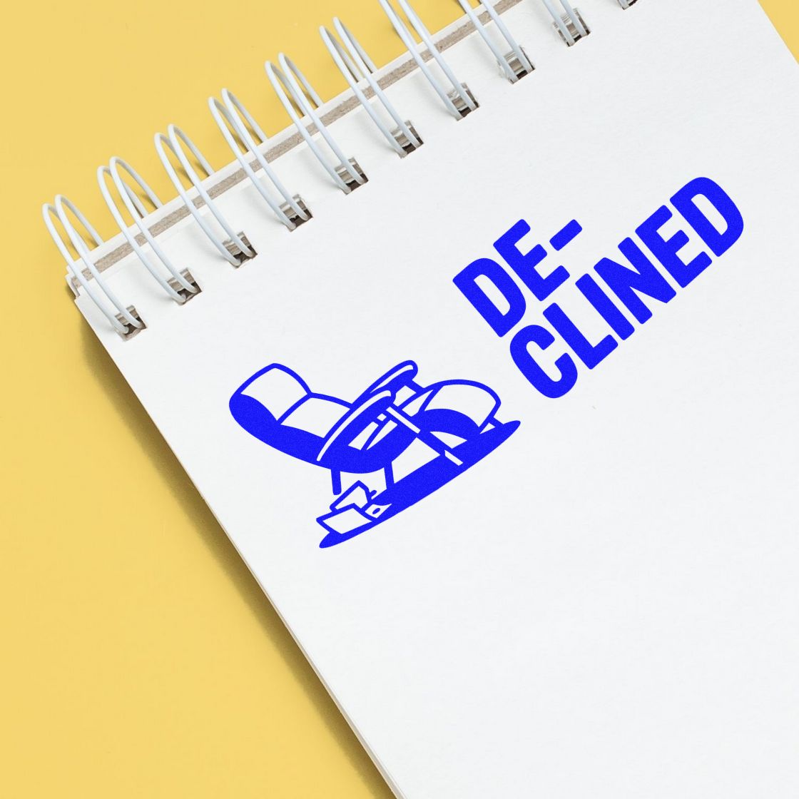 Blue declined stamp and seal on a white spiral notebook with yellow background.
