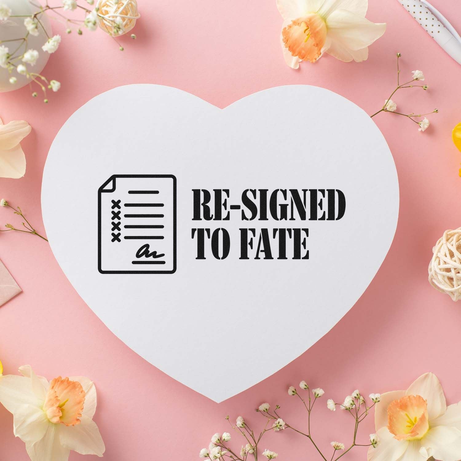 White heart-shaped stamp seal with black RE-SIGNED TO FATE text and document icon on pink floral background.