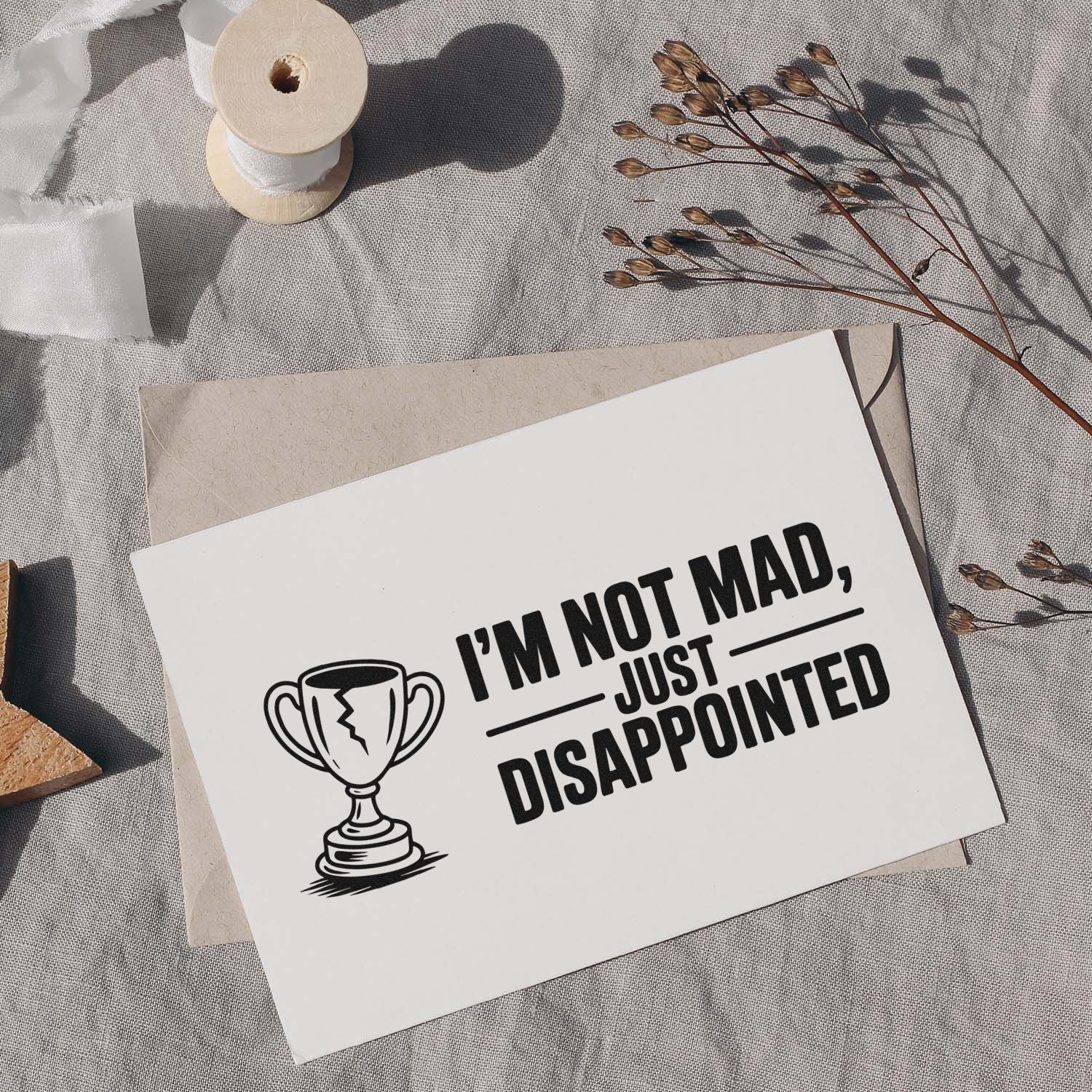 Black custom stamp and seal on white card, reading Im not mad, just disappointed, with trophy icon on a beige envelope.
