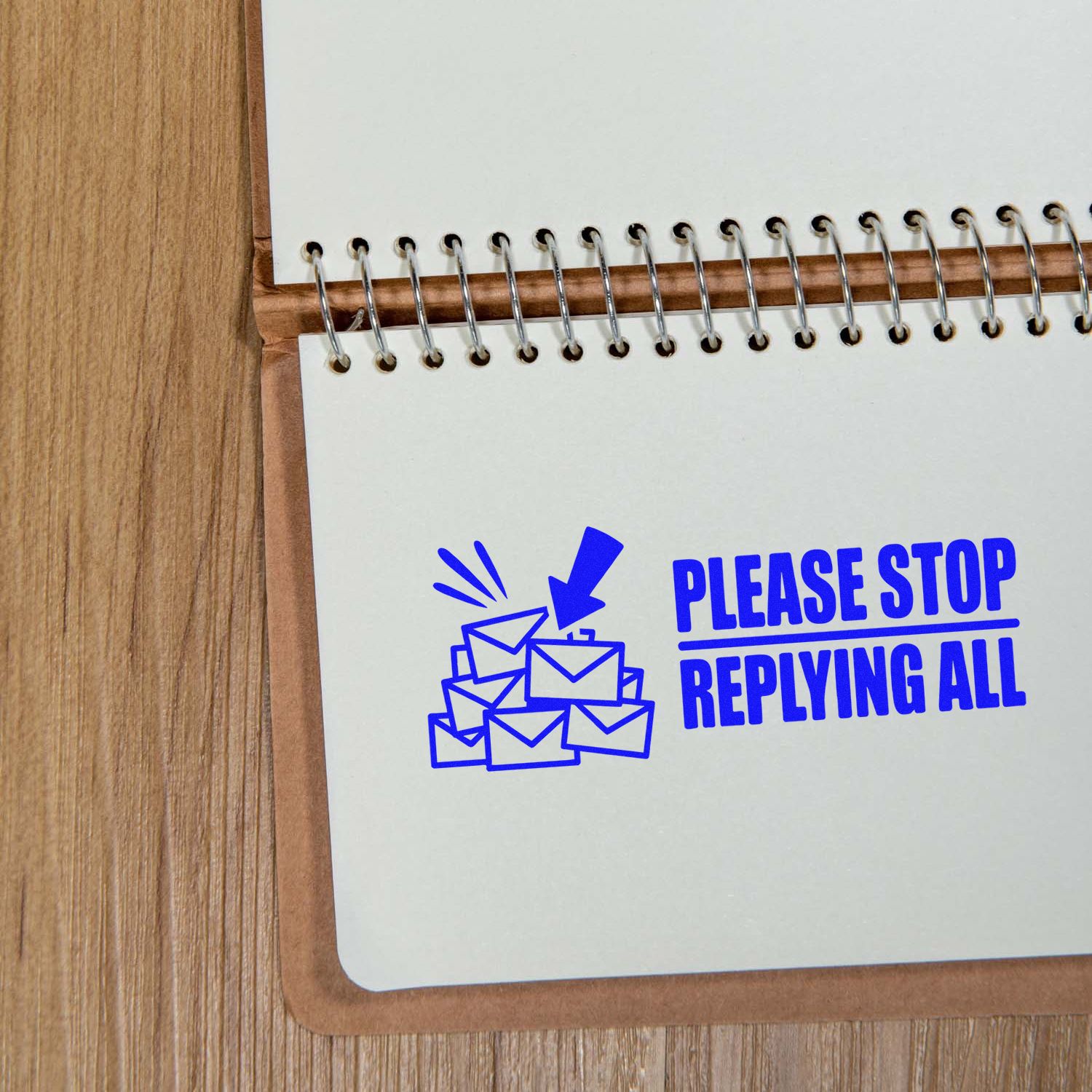 Blue self-inking stamp seal reading PLEASE STOP REPLYING ALL with envelope icon on white spiral notebook.