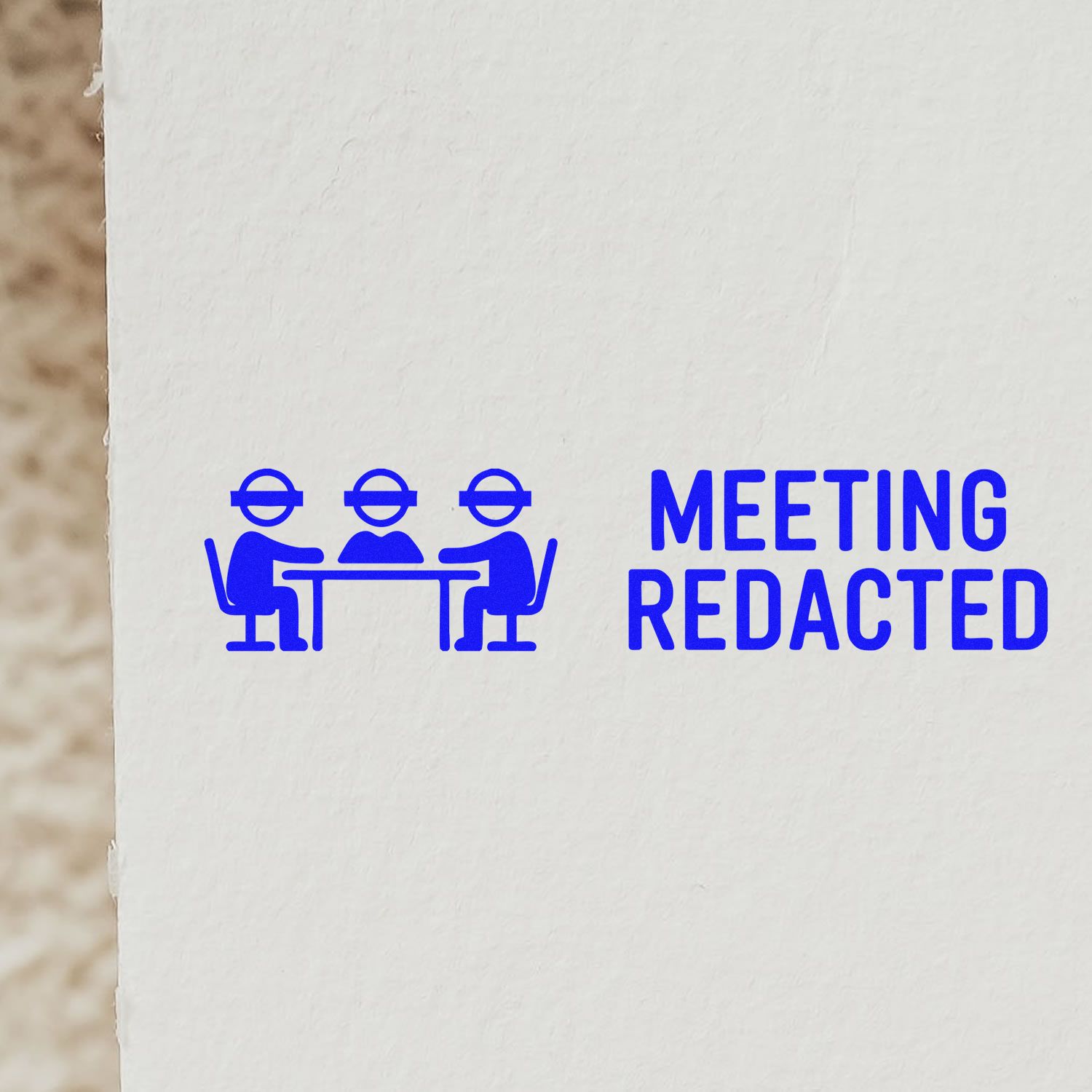 Blue rubber stamp reading MEETING REDACTED with three people at a table on white paper.