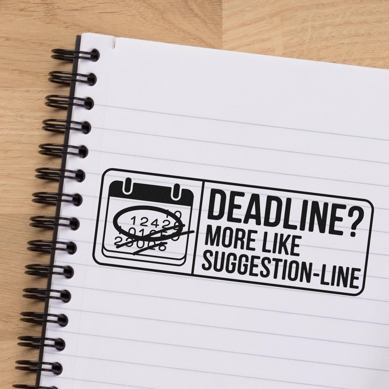 Black stamp and seal reading Deadline? More like suggestion-line on a white spiral notebook over a wood desk.