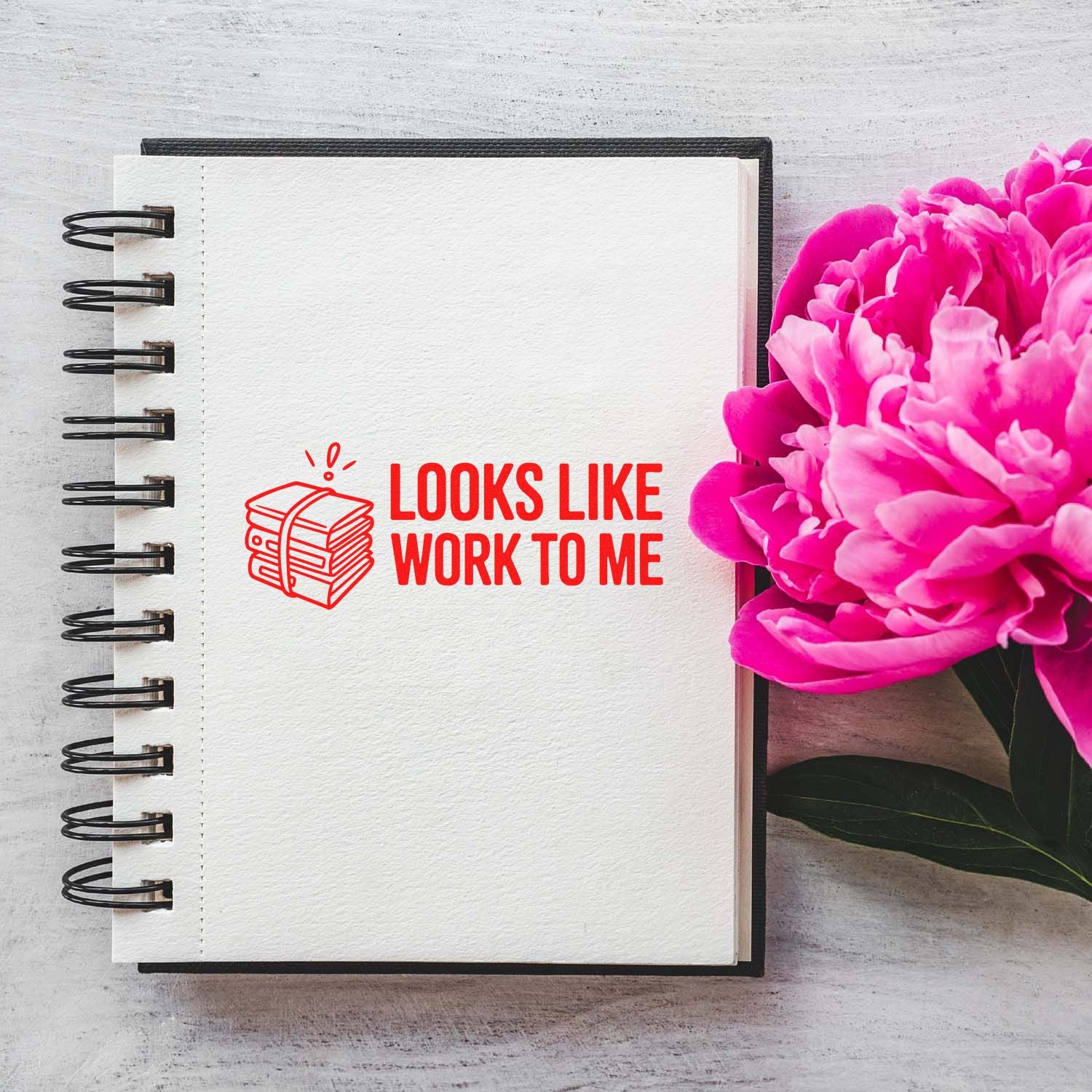 Red work stamp and seal reading Looks like work to me on a spiral notebook beside bright pink flowers.