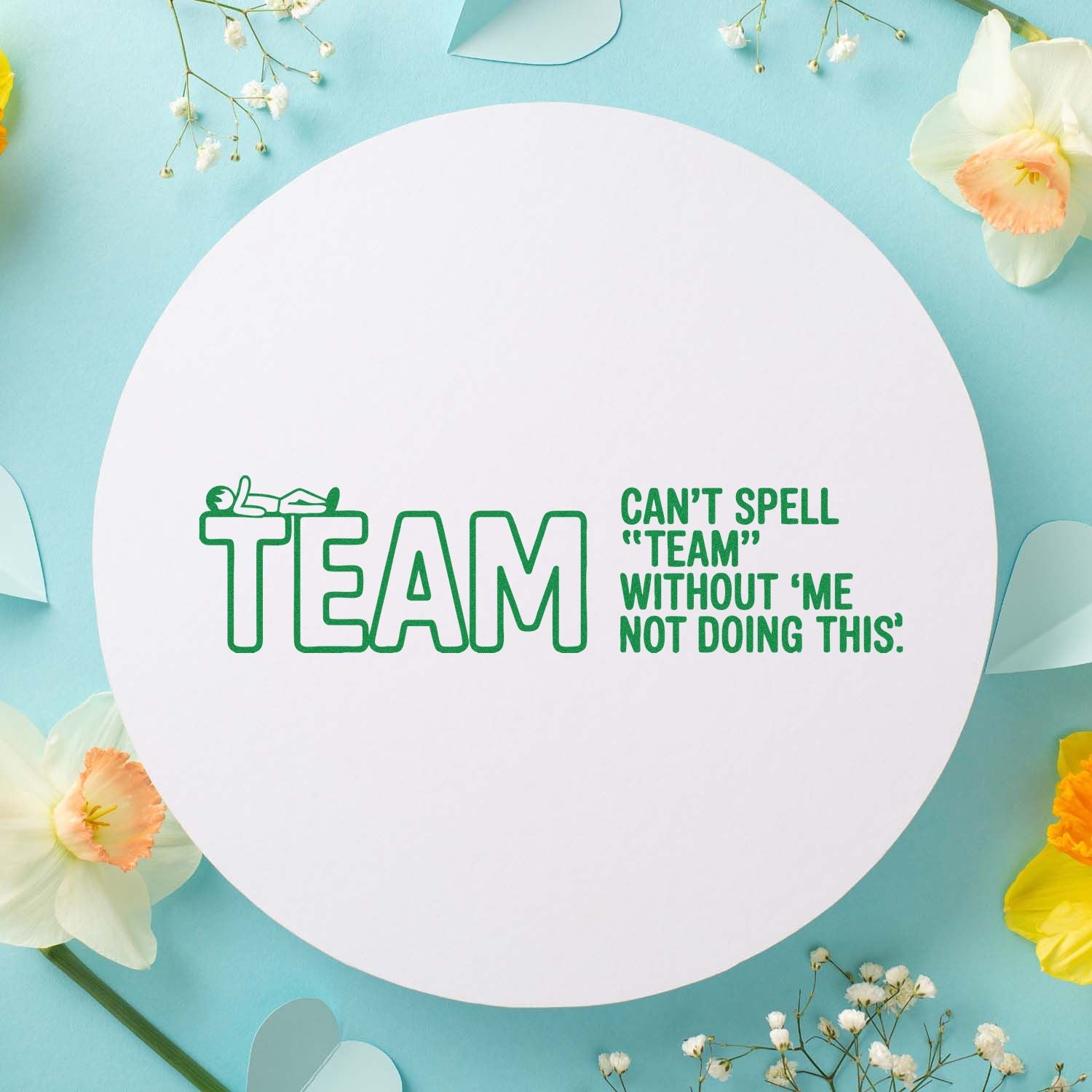 Green TEAM stamp and seal with humorous quote on a white circle, set against a soft blue floral background.