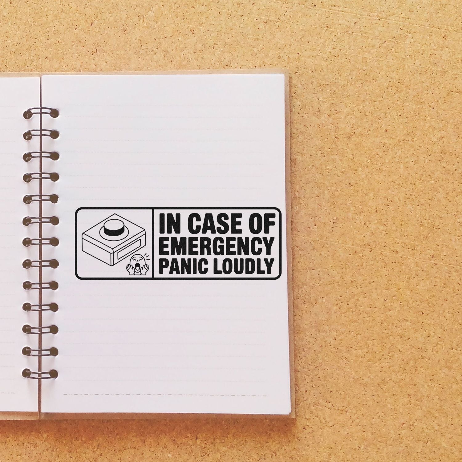 Black stamp seal with In Case of Emergency Panic Loudly on a white spiral notebook, set against a tan textured background.