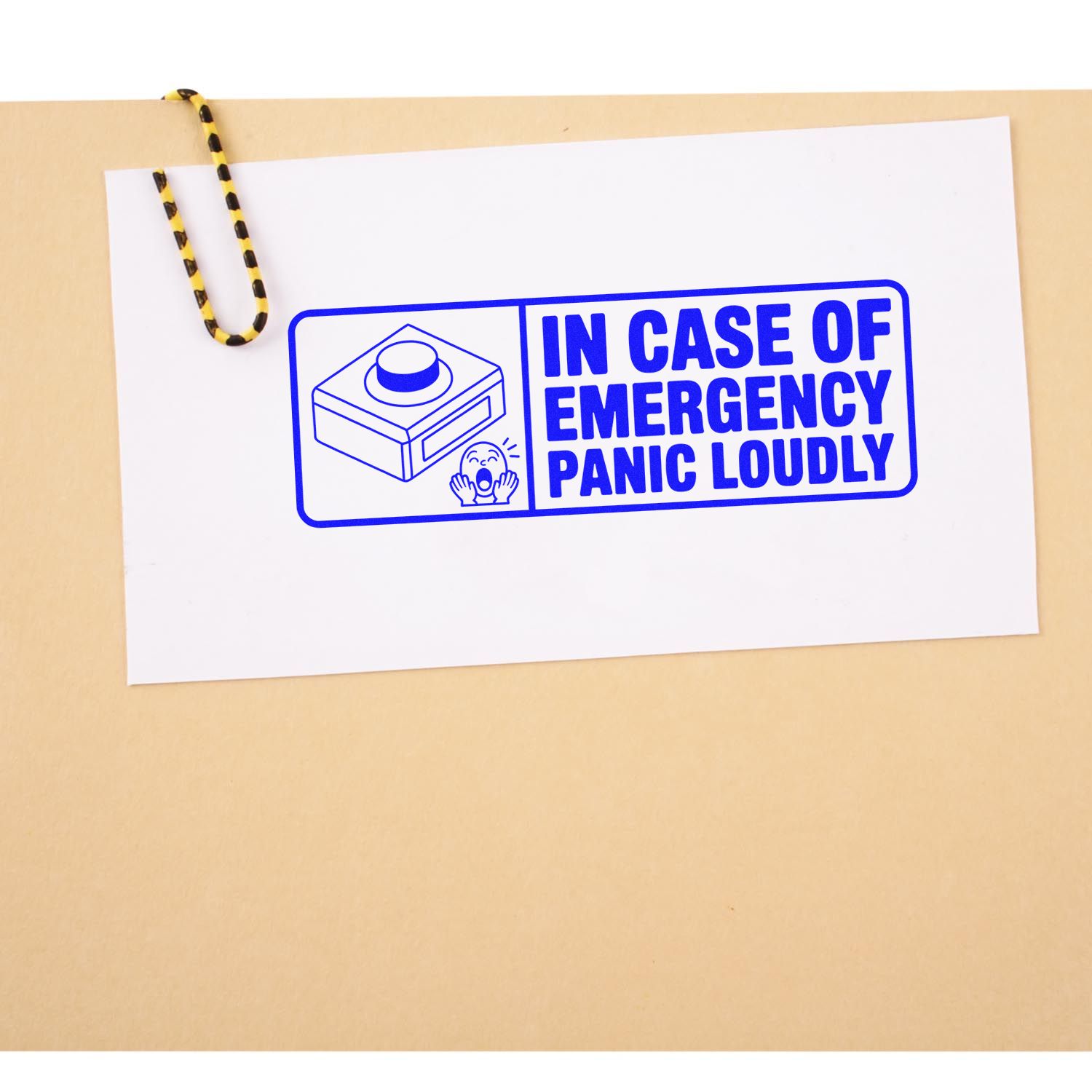 Blue emergency stamp seal on white card with paper clip, reading In Case of Emergency Panic Loudly, on beige background.