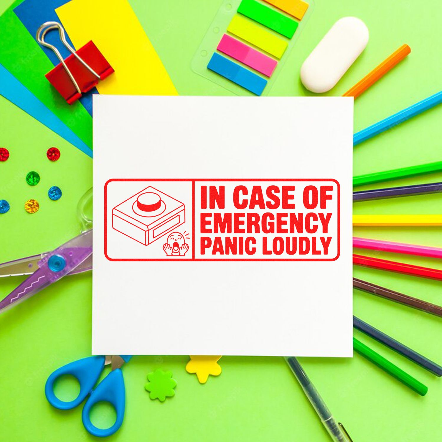 Red rubber stamp seal on white paper reading In Case of Emergency Panic Loudly, surrounded by colorful stationery.