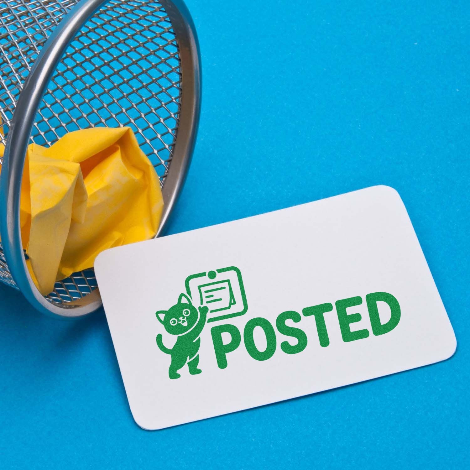 White POSTED stamp/seal card with green cat logo on blue background beside a metal mesh basket and yellow tissue.