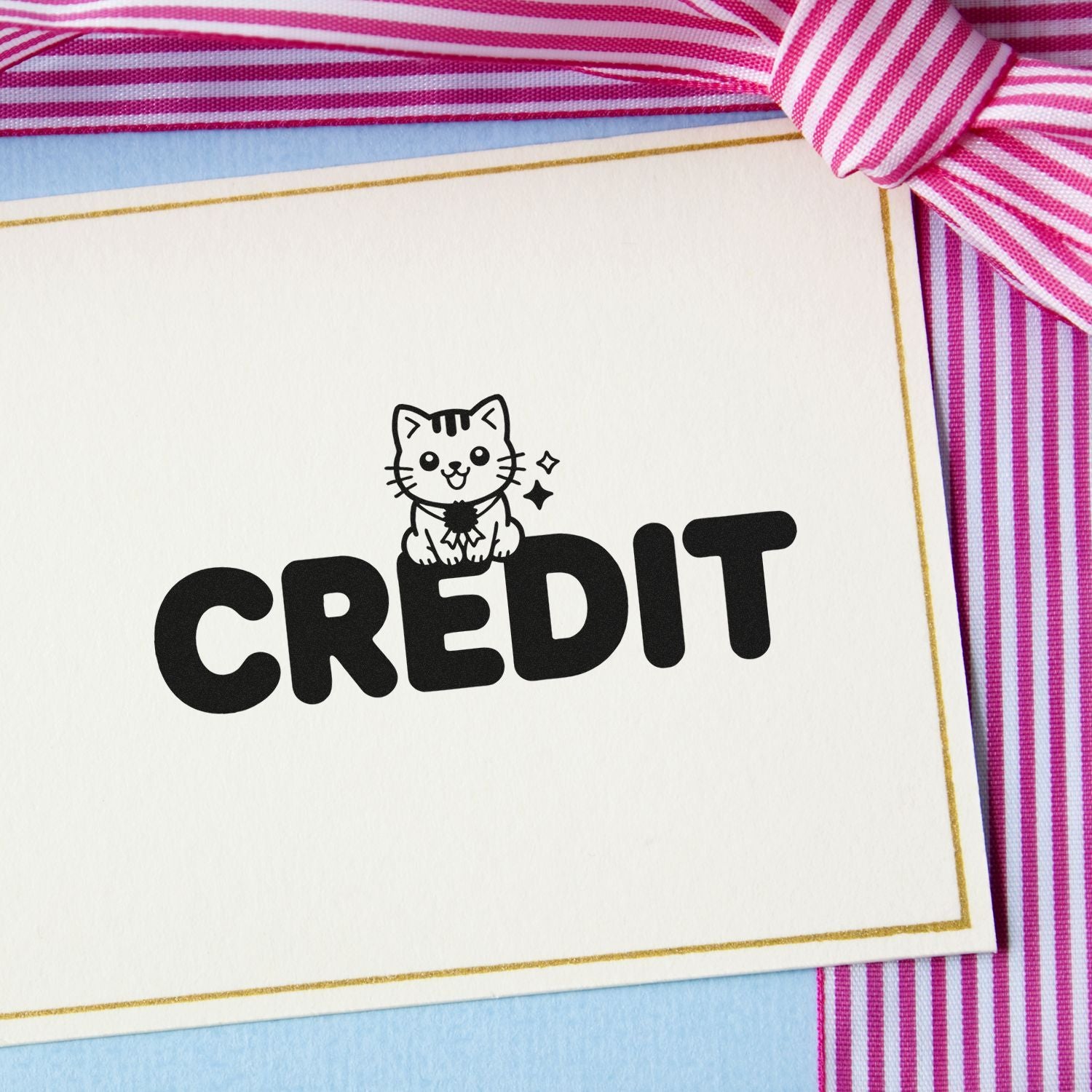 Black CREDIT stamp with cute cat seal on white card, accented by pink striped ribbon, gold trim, and blue backing.