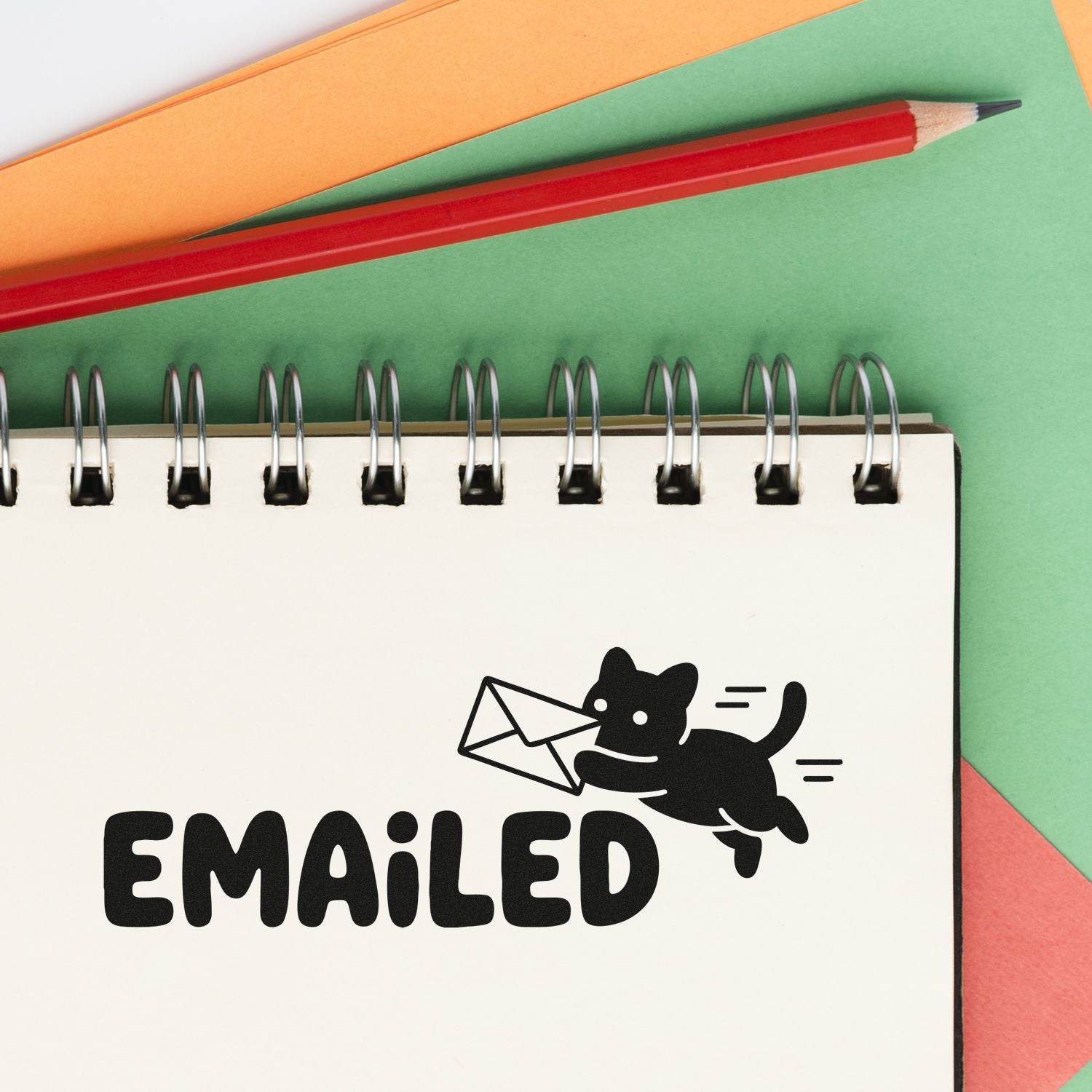 Black Emailed stamp and seal design with cat and envelope on white spiral notebook, over green, orange, and red paper.