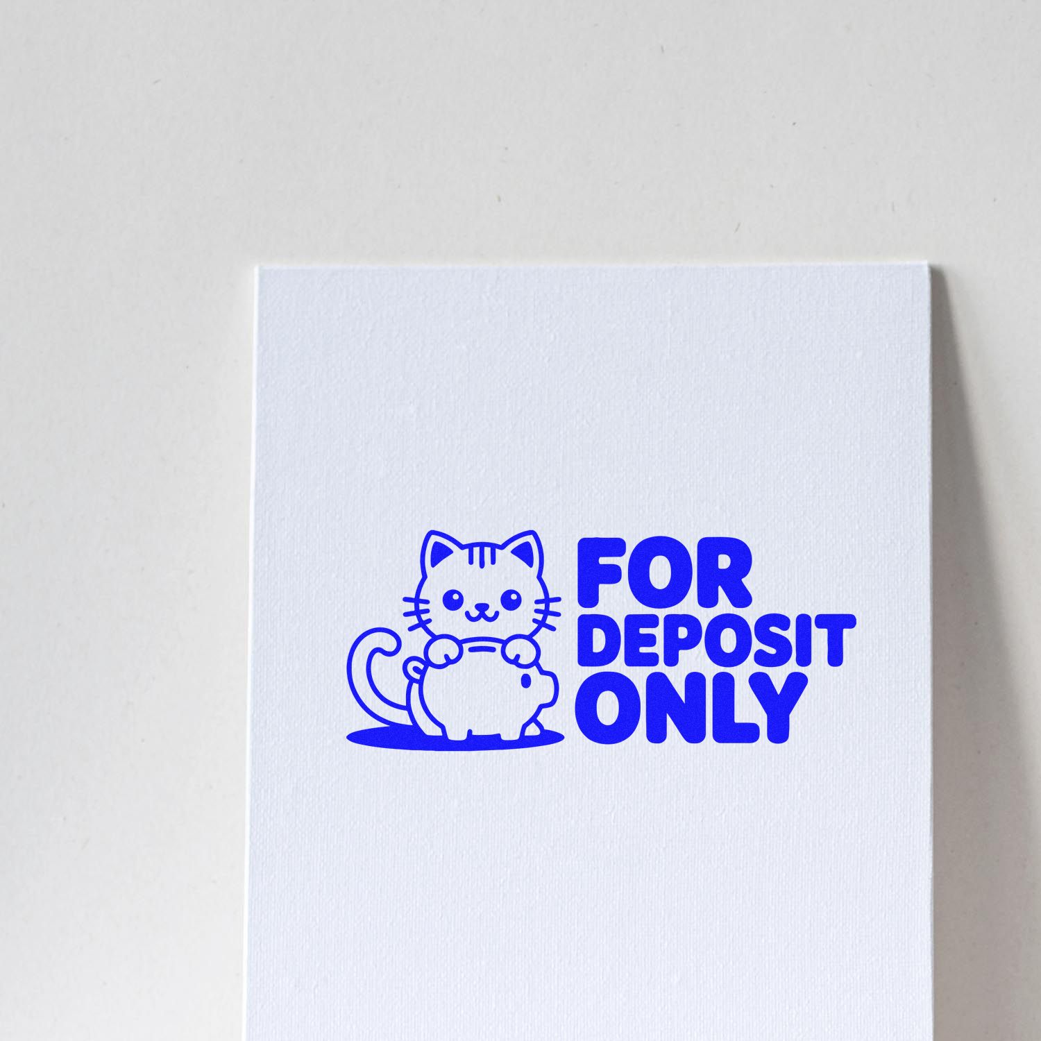 Blue rubber stamp reading FOR DEPOSIT ONLY with cat perched on a piggy bank on white paper.
