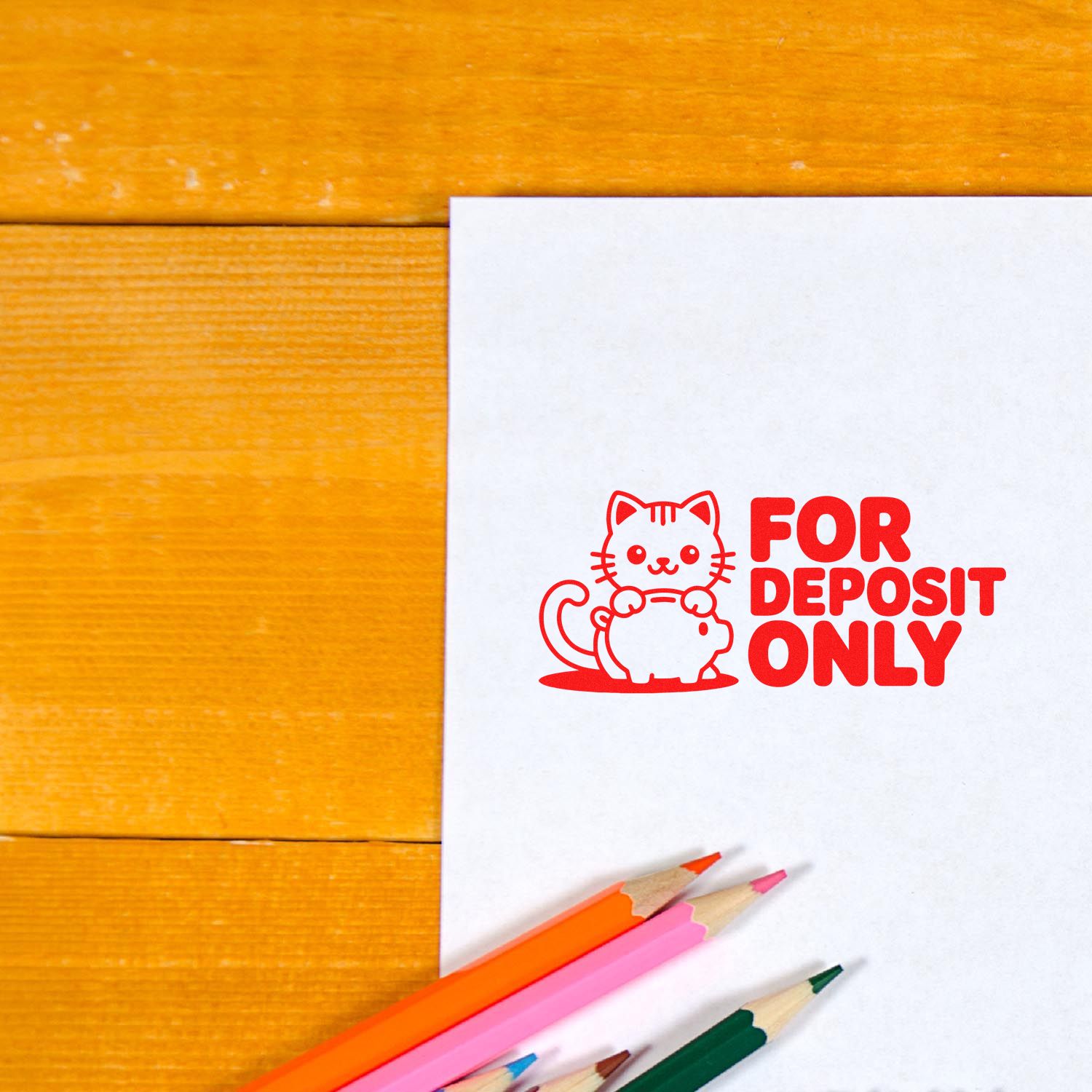 Red For Deposit Only stamp seal with cat graphic on white paper, beside orange, pink, and green pencils on wood.