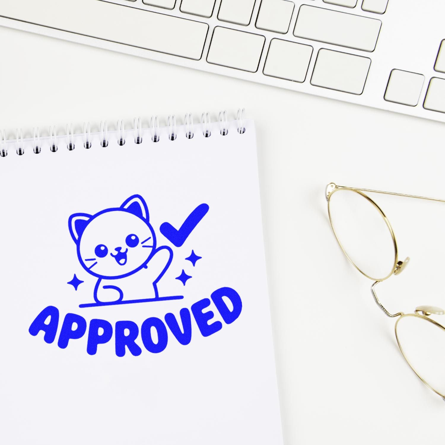 Blue cat APPROVED stamp on white spiral notepad beside keyboard and gold glasses, stamp and seal office product