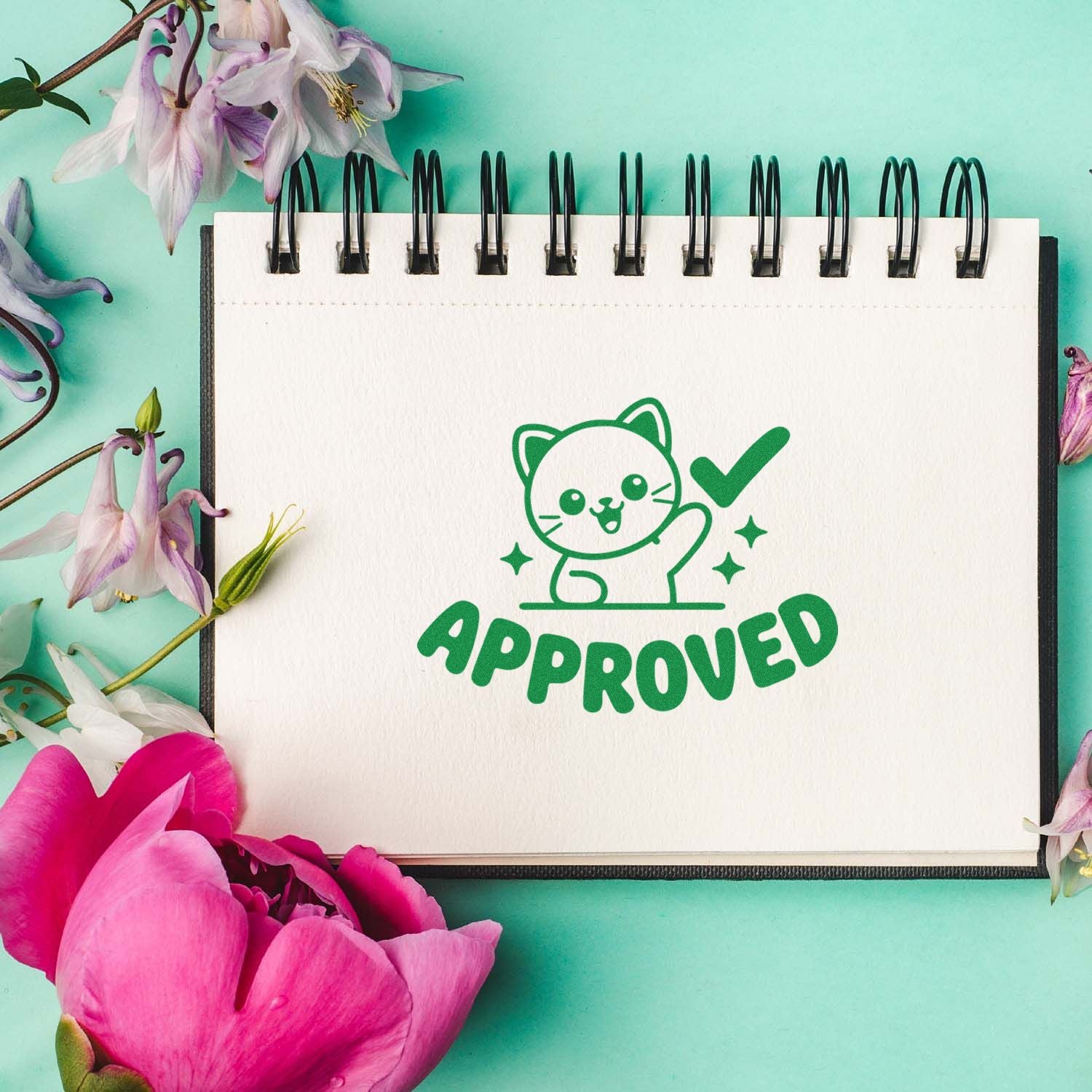 Green approved cat stamp and seal on white spiral notebook, framed by pink and purple flowers on mint background.