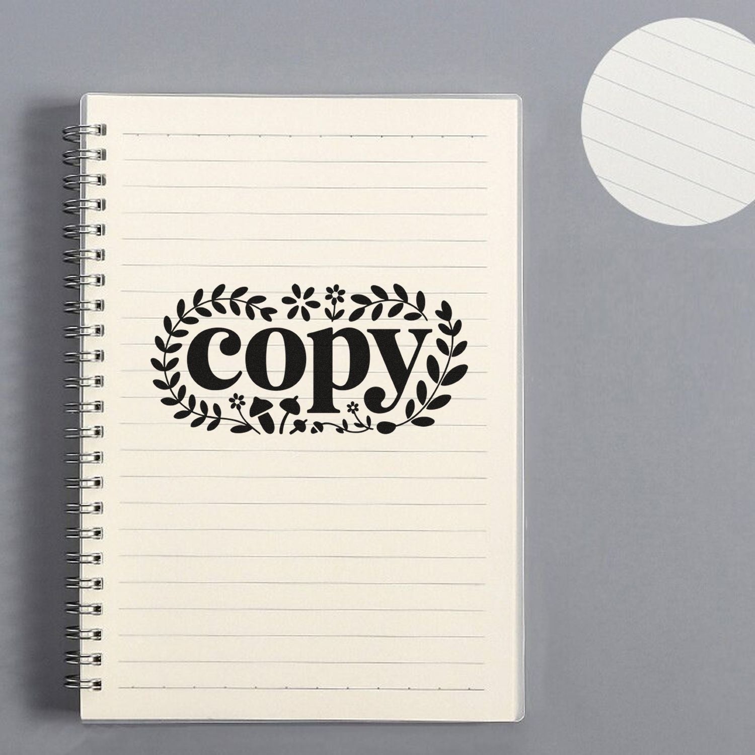 Black floral copy stamp and seal on cream lined spiral notebook, with matching round seal sample on gray background.