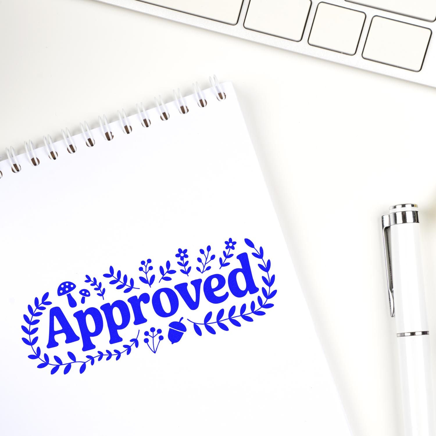 Blue Approved stamp seal with floral wreath on white notepad, beside a white pen and keyboard.
