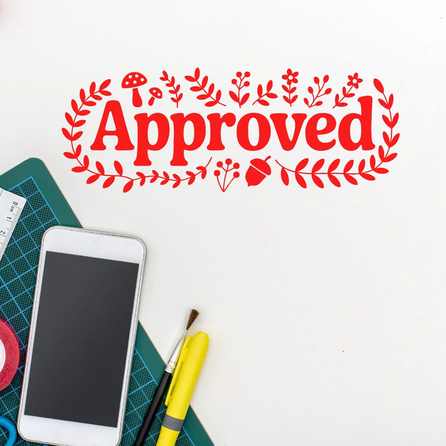 Red Approved rubber stamp seal with floral wreath, beside craft tools on a white background