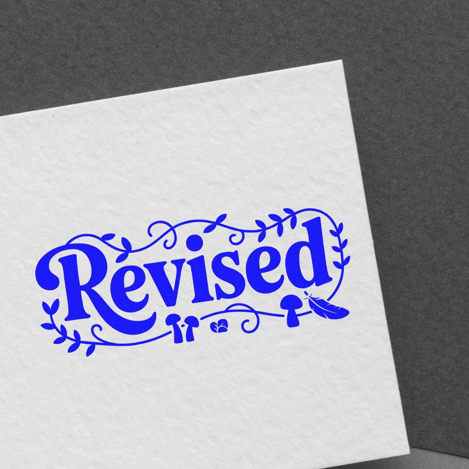 Blue Revised rubber stamp with decorative seal-style leaves and feather on white paper