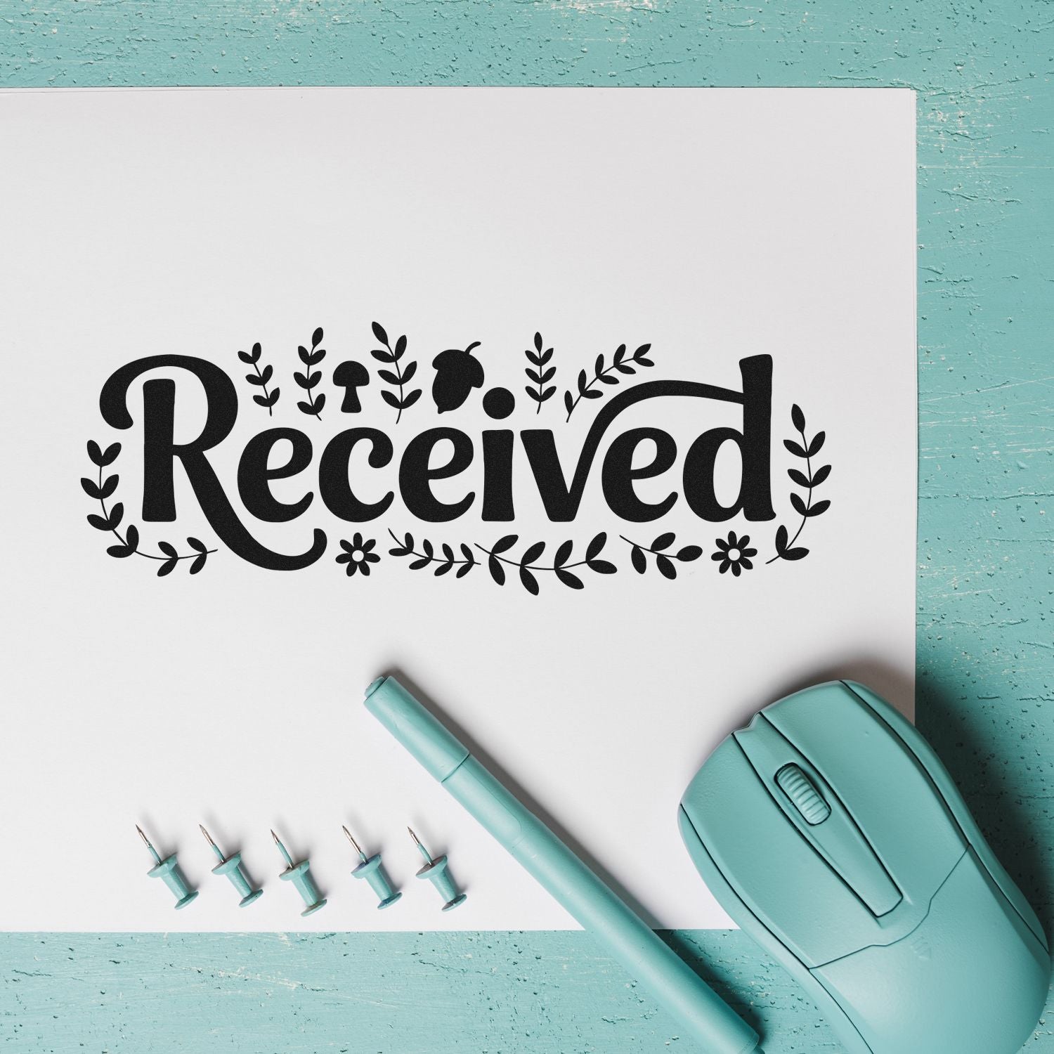 Black floral Received stamp design with teal stamp tool, pen, and pins on white paper and aqua background.