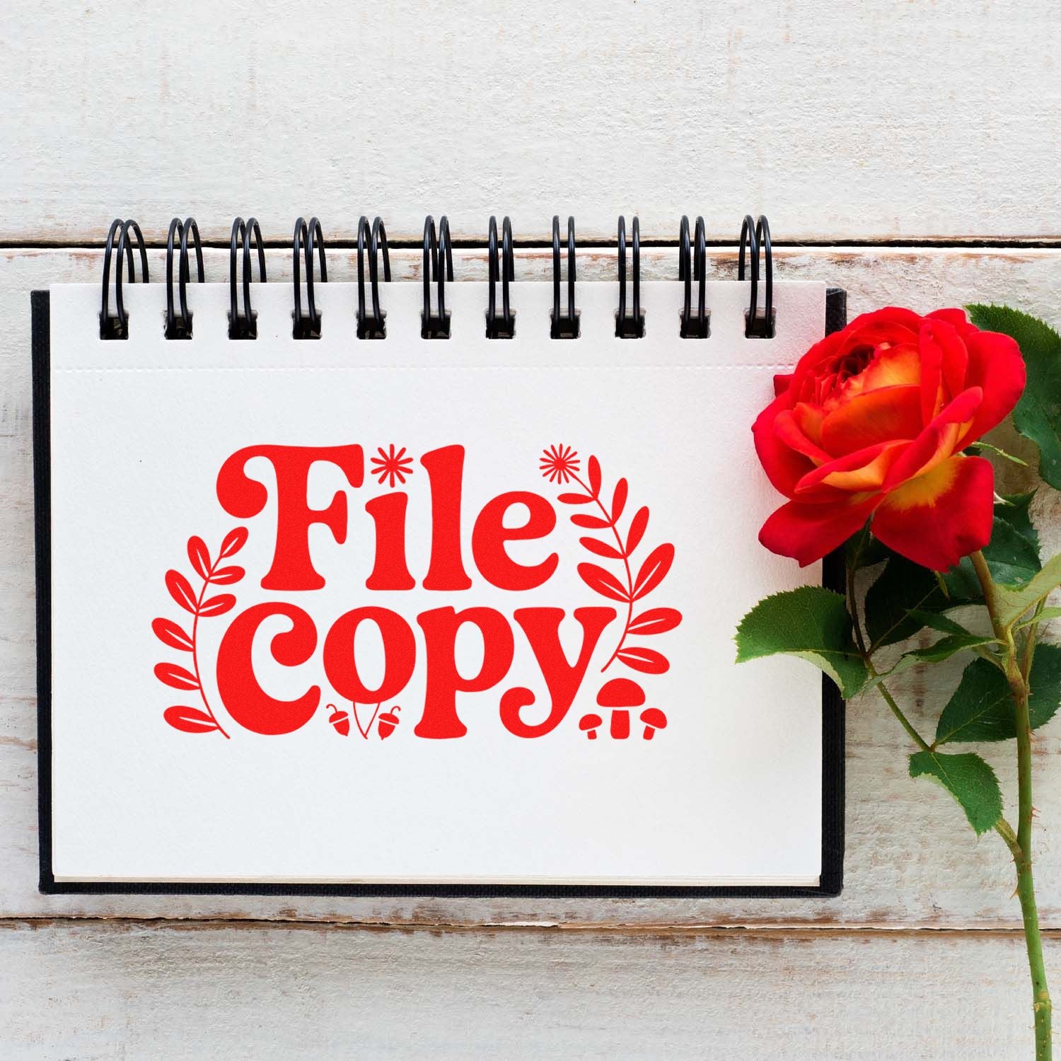 Red File Copy stamp-style seal on white spiral notebook beside a red rose, showcasing stamp and seal product design.