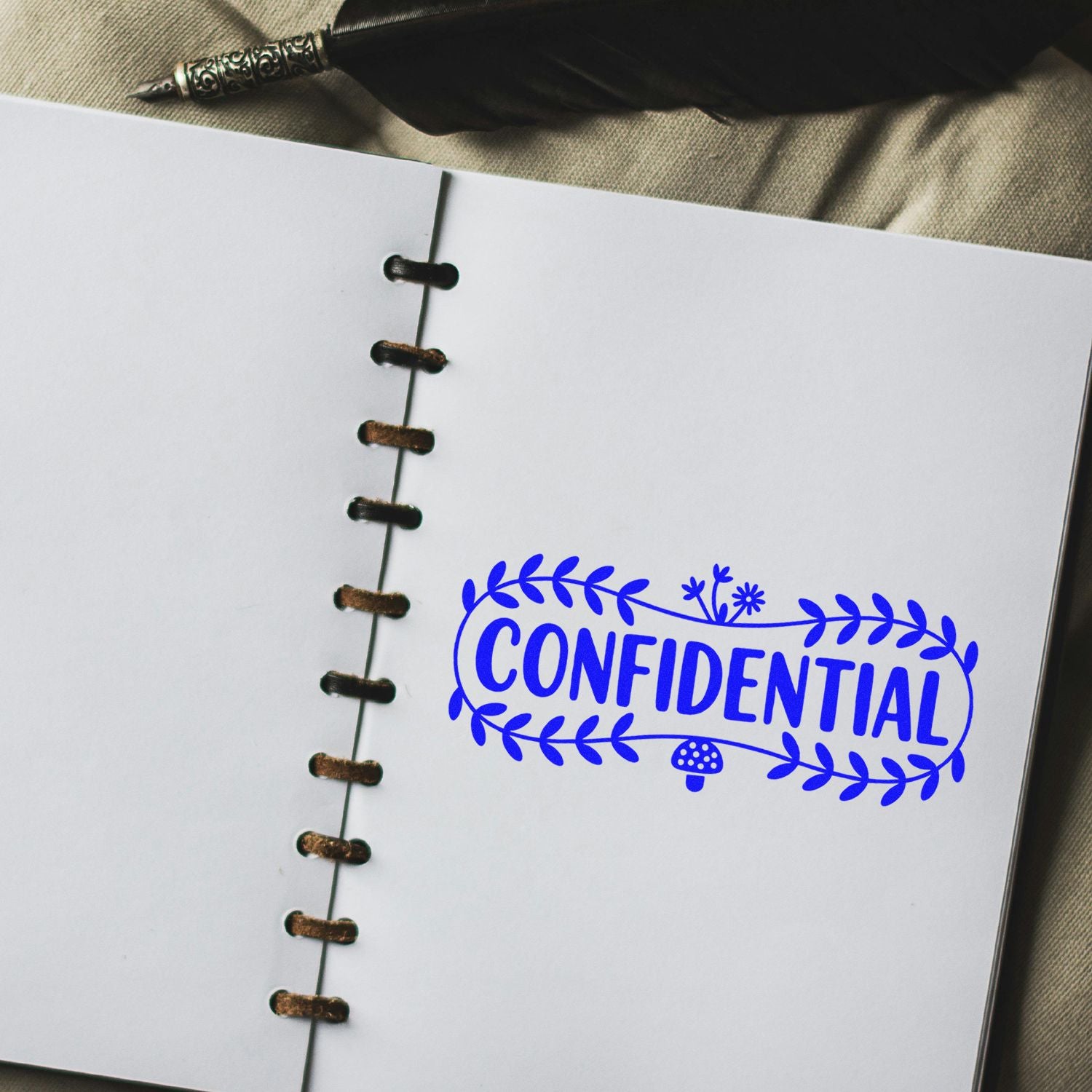 Blue CONFIDENTIAL rubber stamp seal on white notebook page with brown stitched binding and black quill pen.