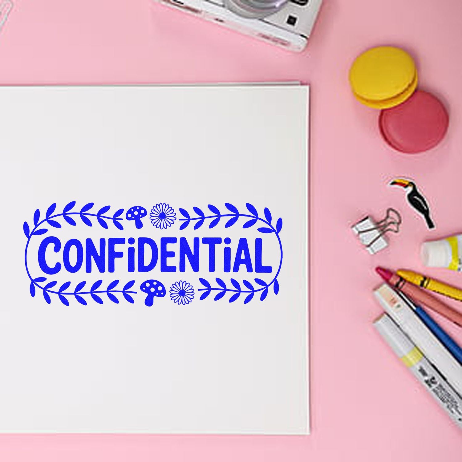 Blue confidential stamp on white paper with leaf border, pink background, seal pads, and marking tools