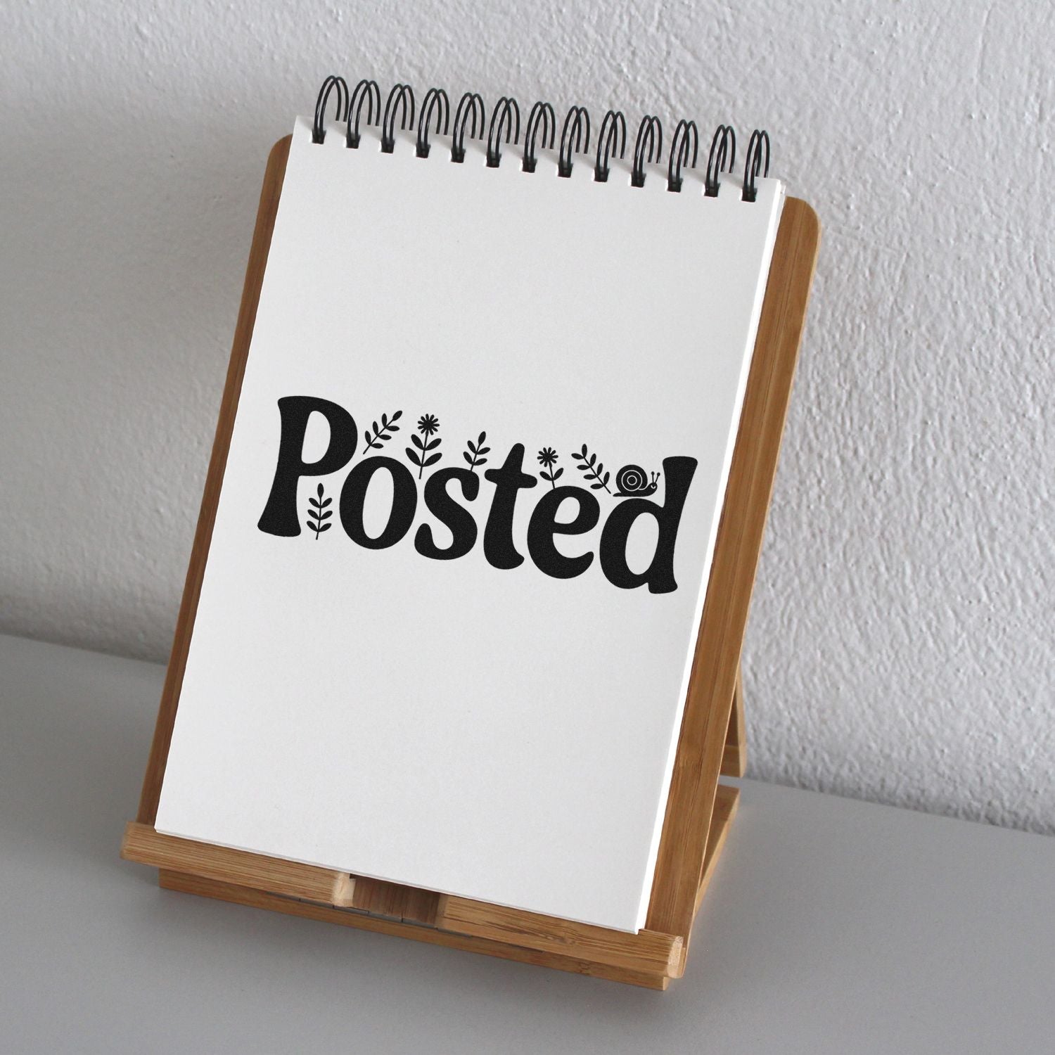 White spiral notepad on wooden stand with black Posted floral stamp seal design