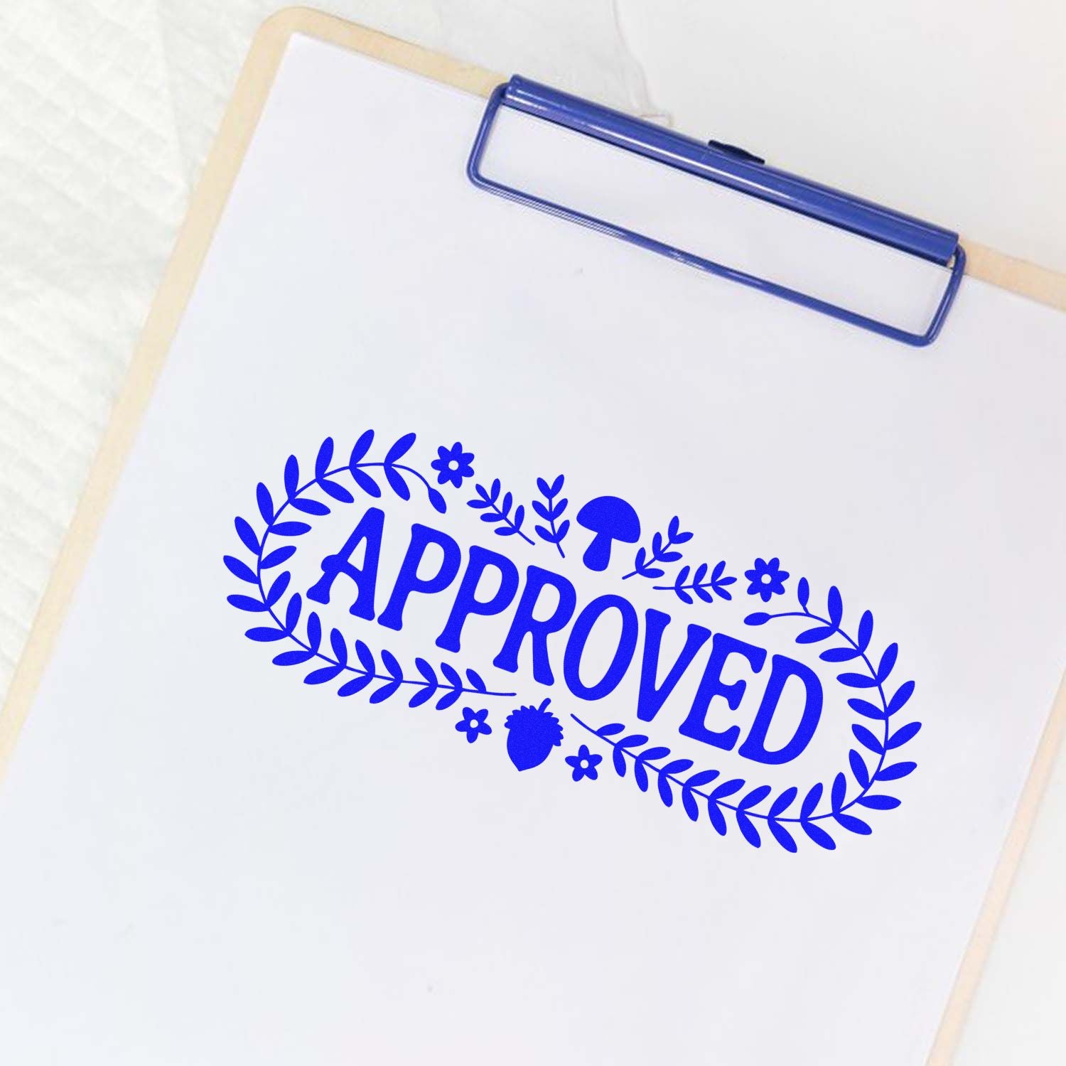 Blue APPROVED stamp seal with leafy wreath on a white clipboard and paper.