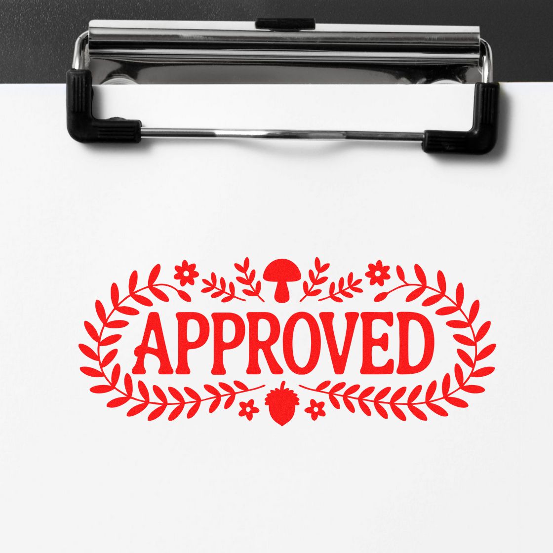 Red APPROVED stamp seal with leaf wreath on white paper clipped to a black-and-silver clipboard.