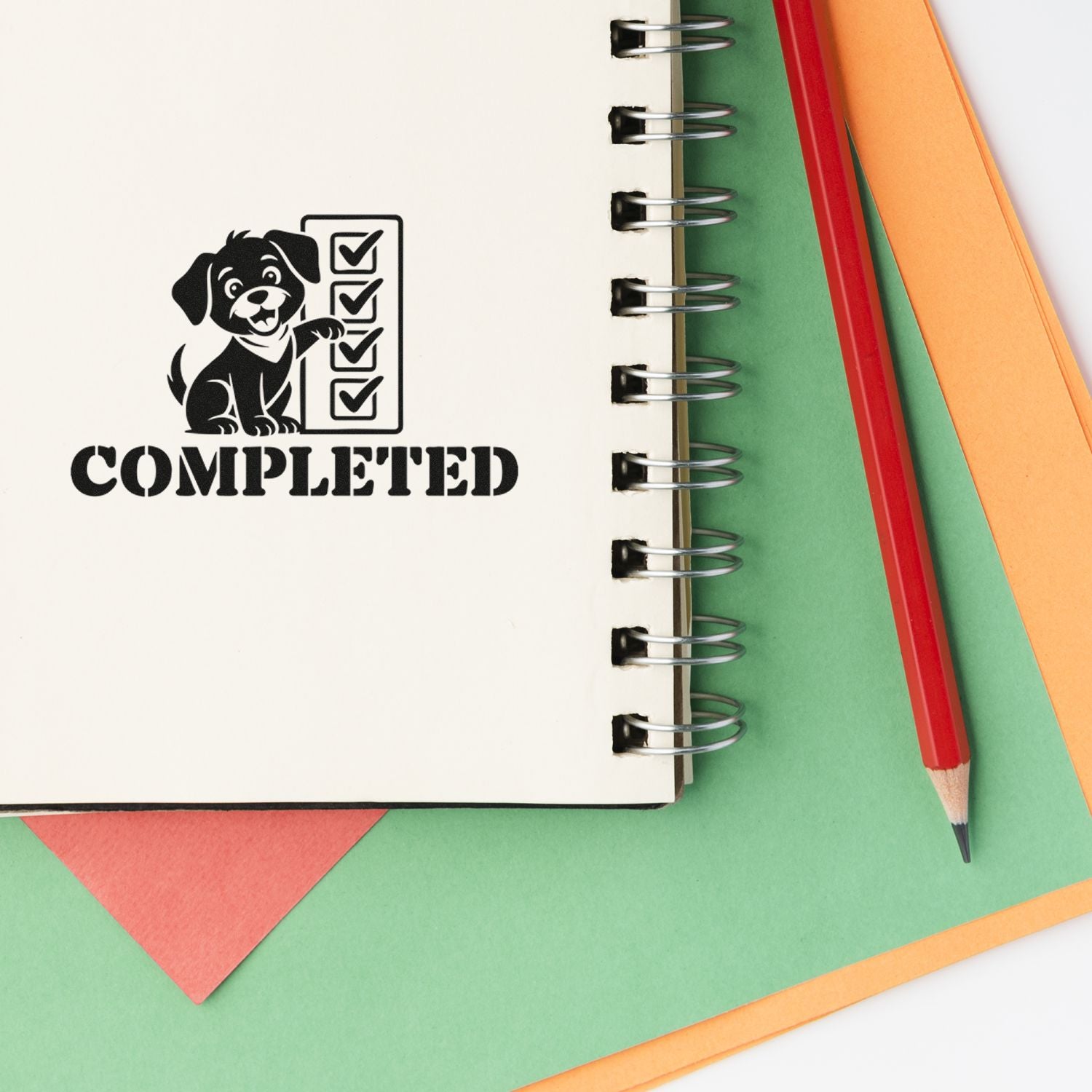Black completed rubber stamp with dog and checklist on white spiral notebook, beside red pencil, green and orange paper.
