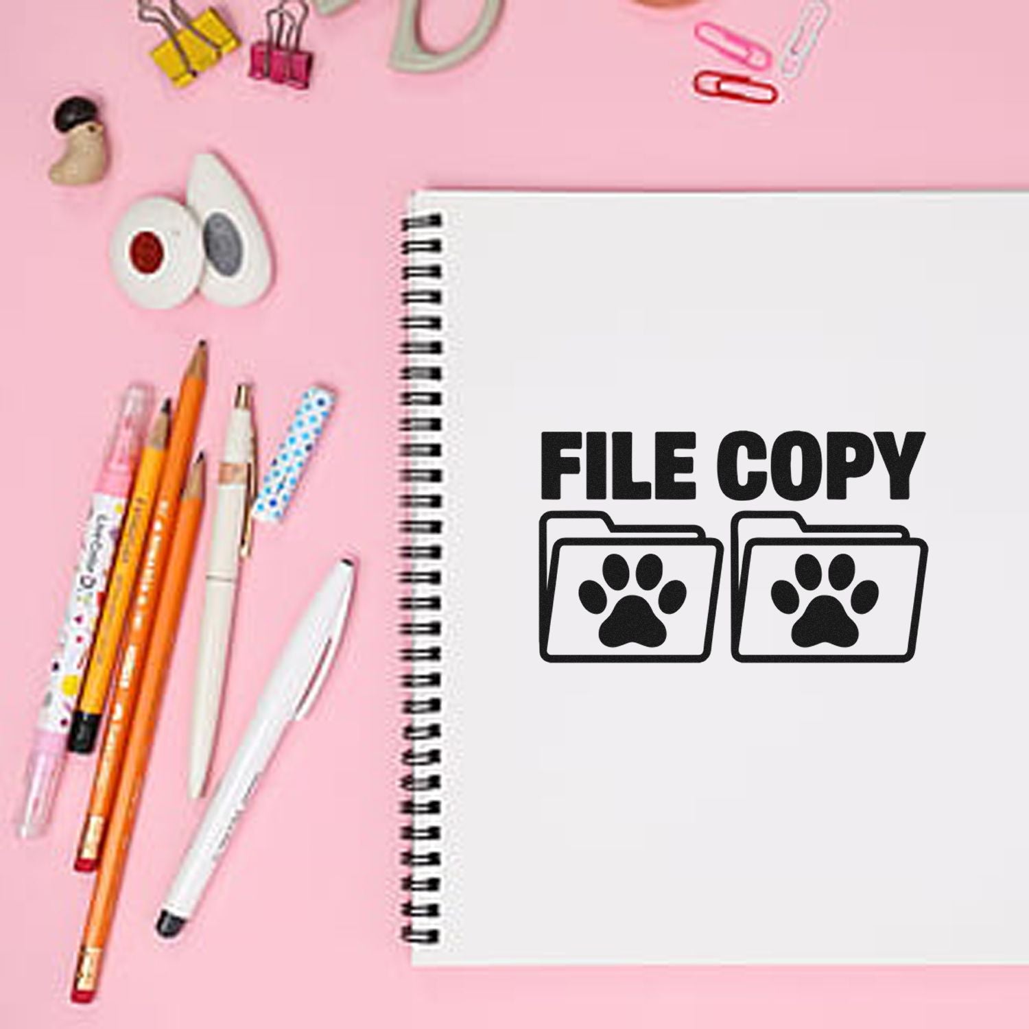 Pink flat lay of stamp and seal products, with spiral notebook, FILE COPY paw-print stamp, pens, and binder clips