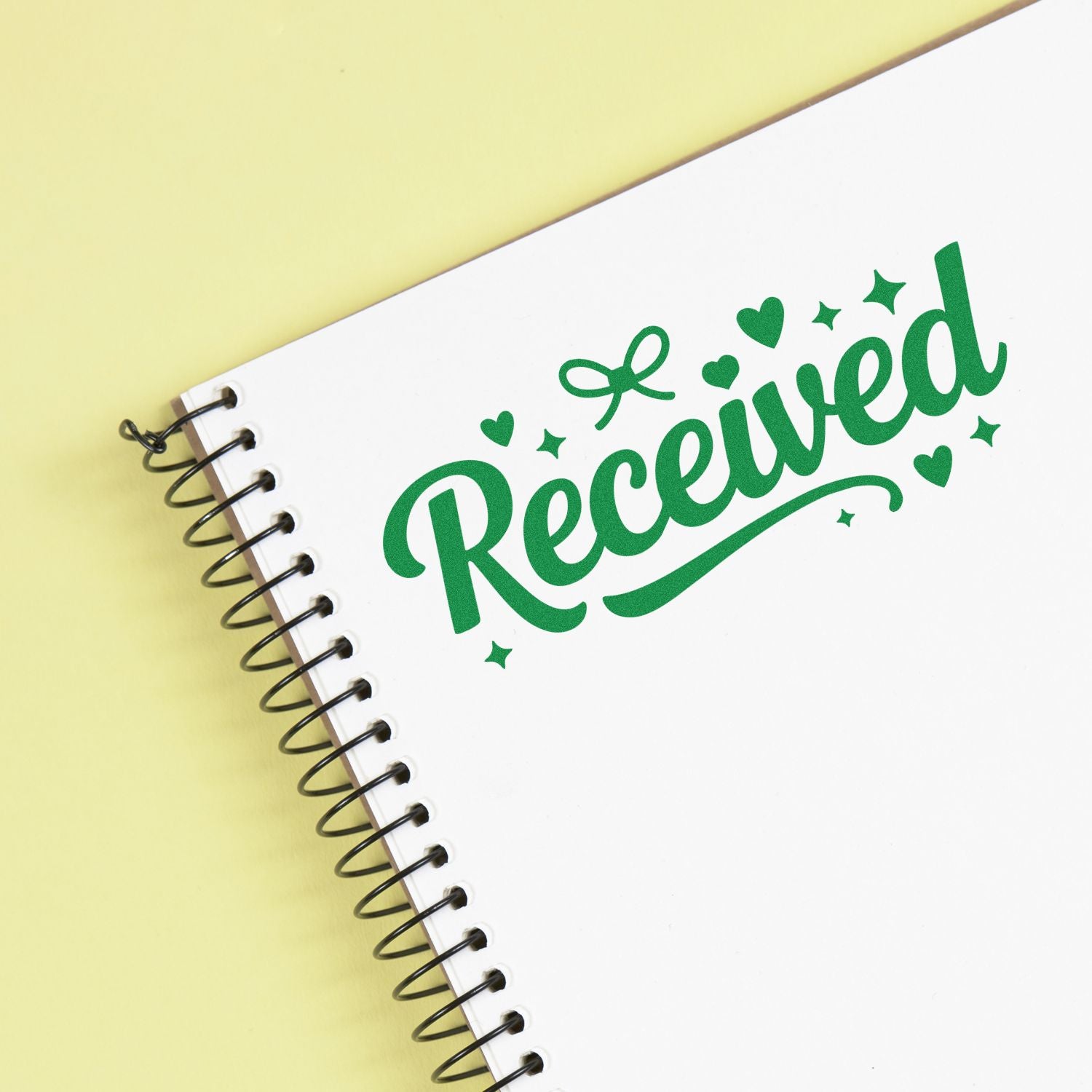 White spiral notebook with green Received stamp seal, heart accents, on pale yellow background