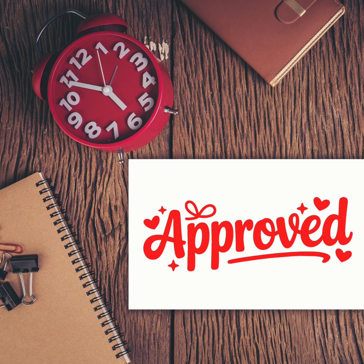 Red Approved stamp and seal on white card, with red alarm clock and notebook on a wood desk