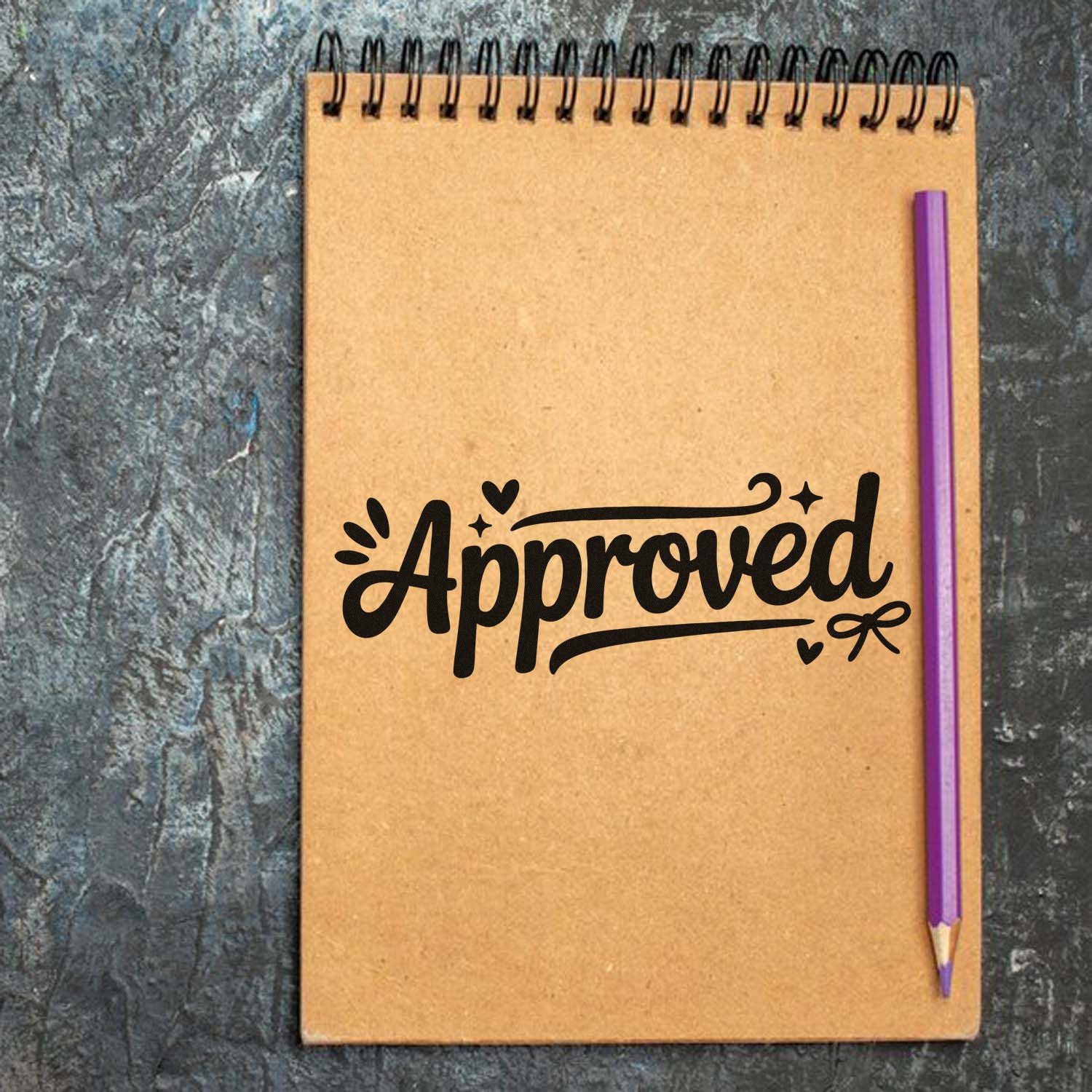 Black Approved stamp on a tan spiral notebook with a purple pencil on a dark textured background.