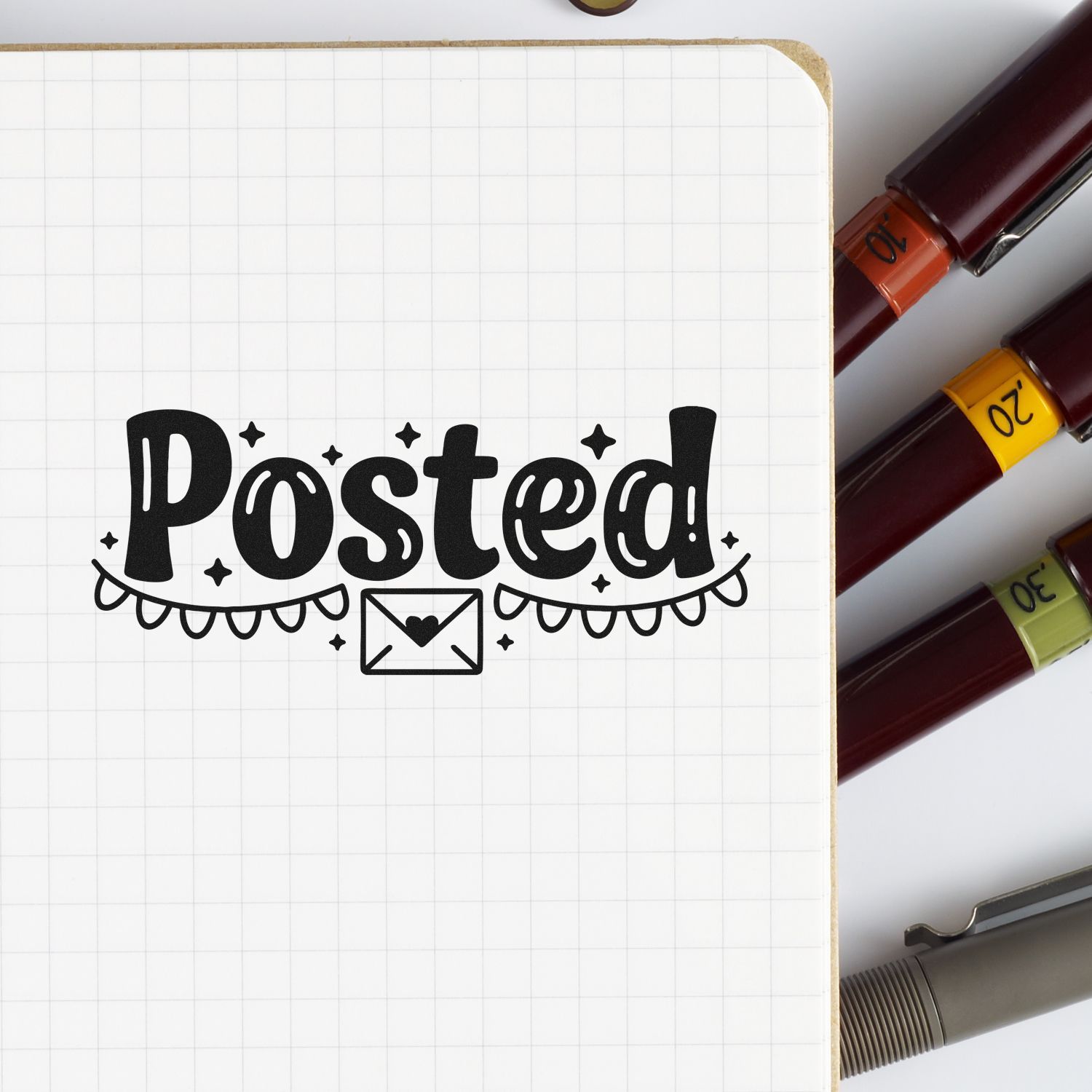 Black Posted! stamp with envelope icon on graph paper, beside burgundy stamp and seal markers with orange, yellow, and green caps.