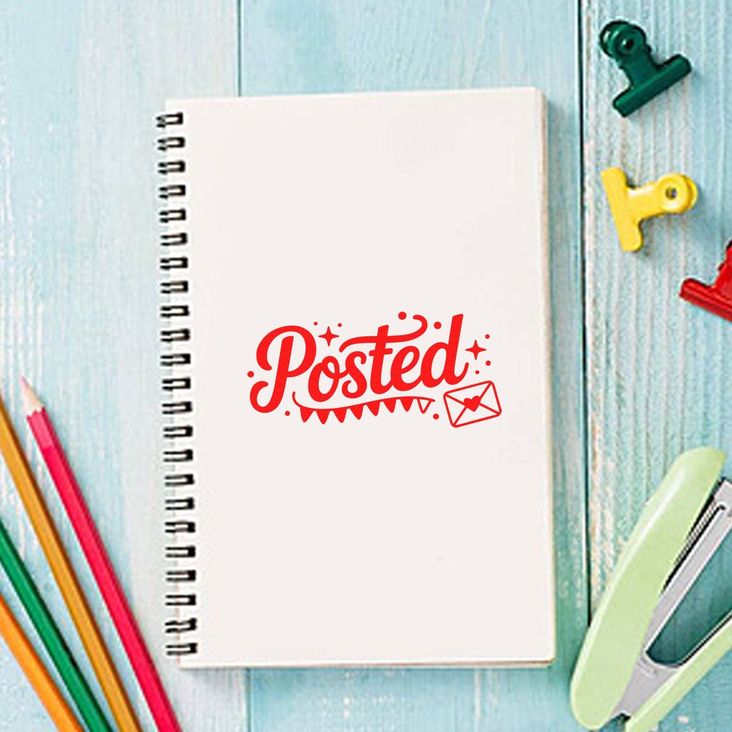 Red Posted stamp seal on a white spiral notebook, with colorful stationery on a pale blue wood background.