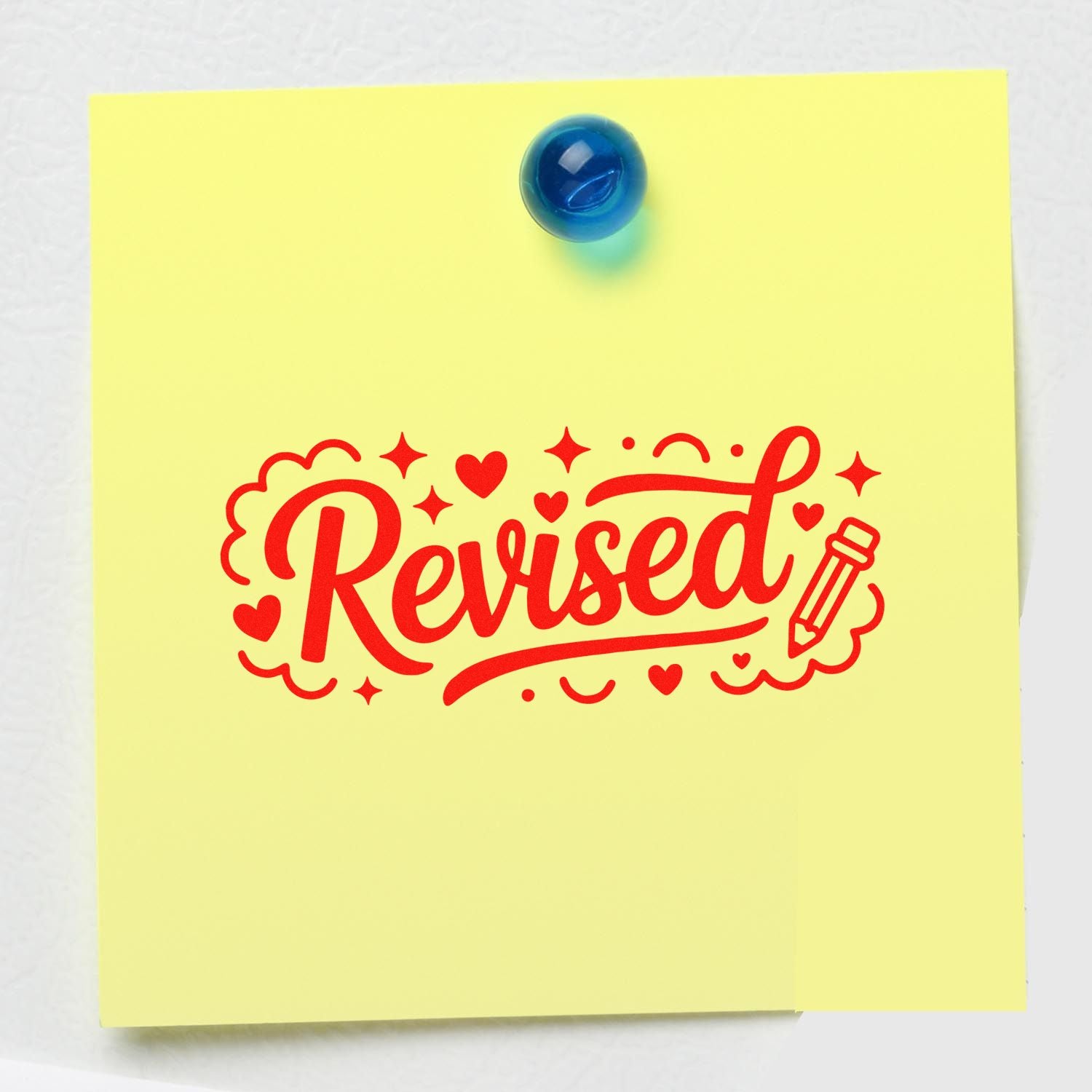 Yellow sticky note with red Revised rubber stamp graphic, hearts and pencil, pinned by a blue pushpin.
