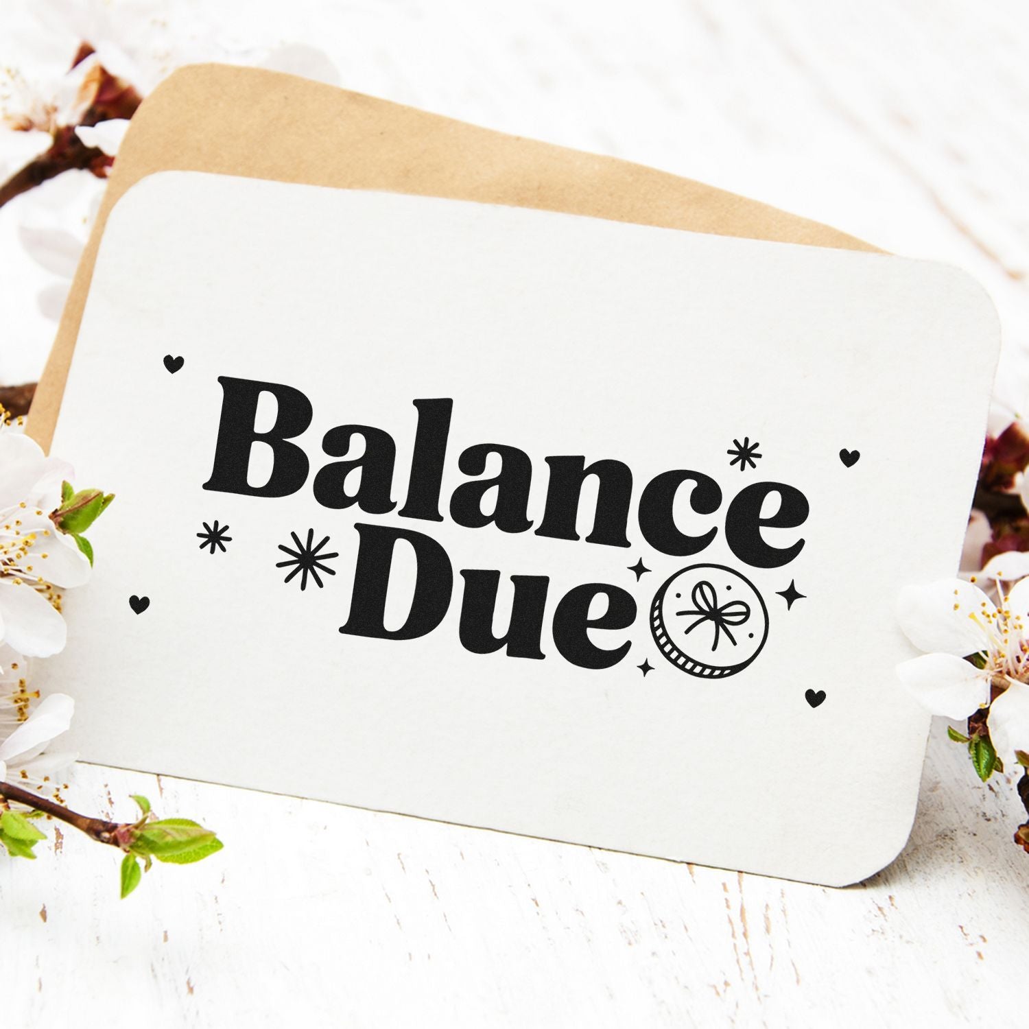 Black Balance Due stamp and seal on white card with hearts and starbursts, layered over tan kraft paper and blossoms