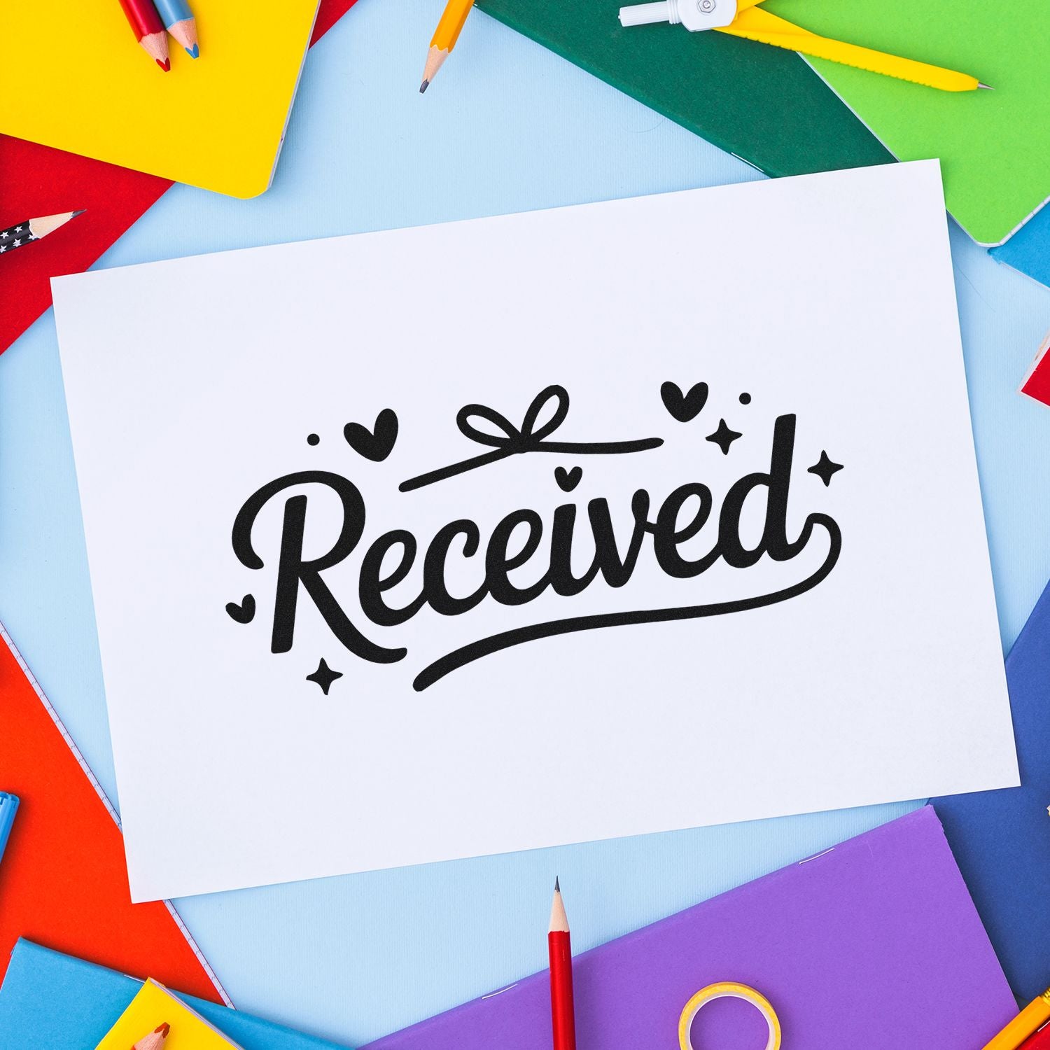 Black Received stamp with hearts and stars on white paper, framed by colorful notebooks and pencils.