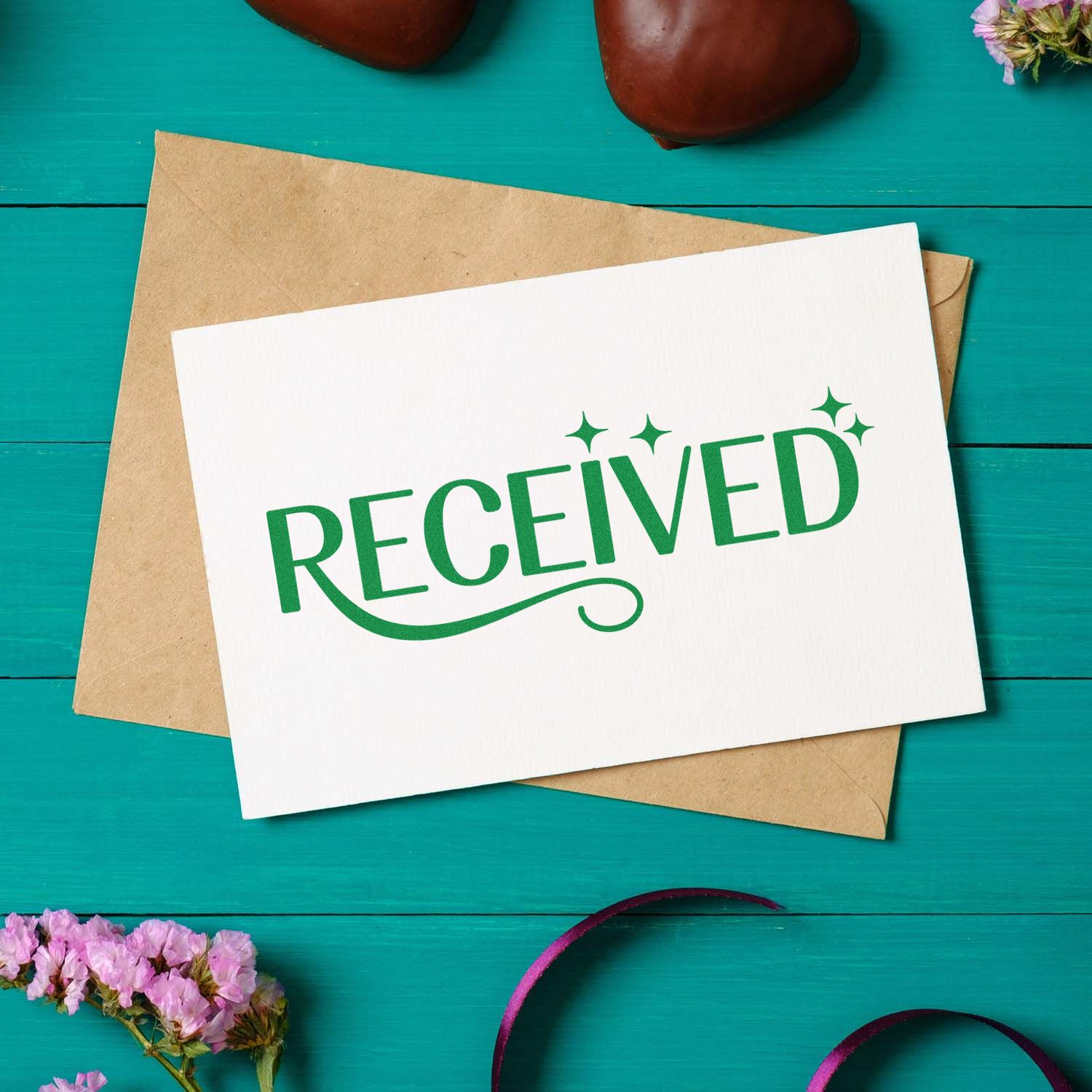 Green RECEIVED stamp and seal on white card over kraft envelope, set on a teal wooden background.