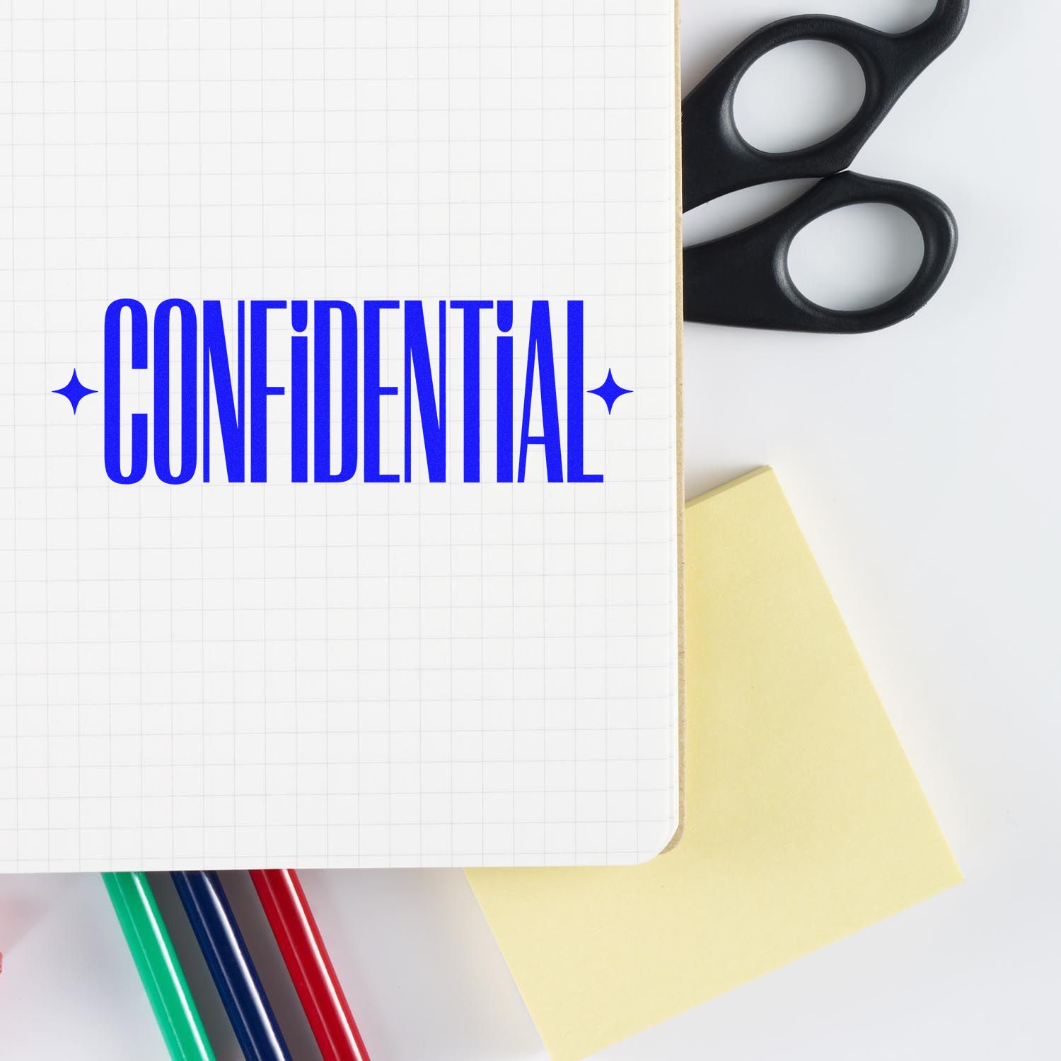 Blue CONFIDENTIAL stamp on grid notebook with black scissors, yellow sticky note and colored pens.