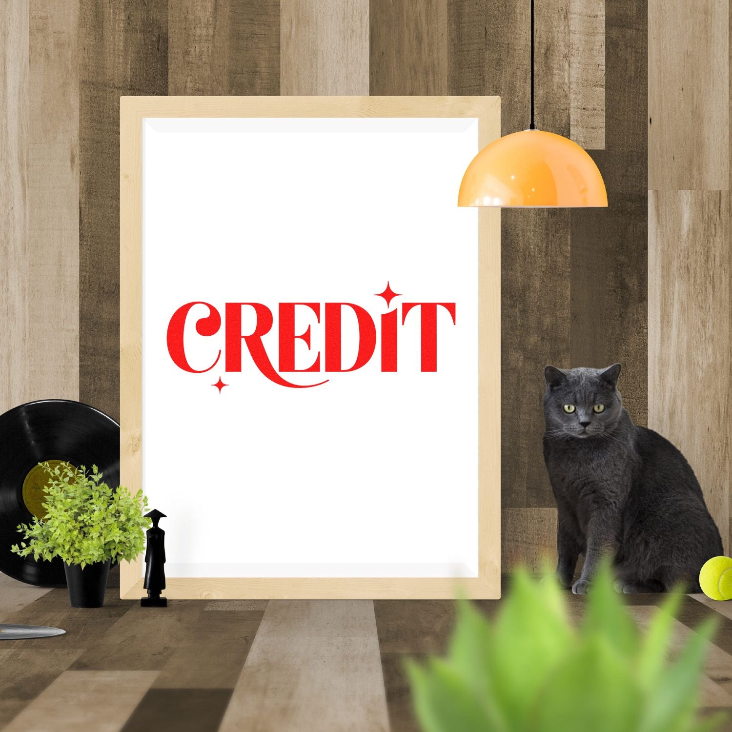 Stamp and seal product mockup with red CREDIT stamp-style text on a white framed poster, wood wall, orange lamp, and black cat.