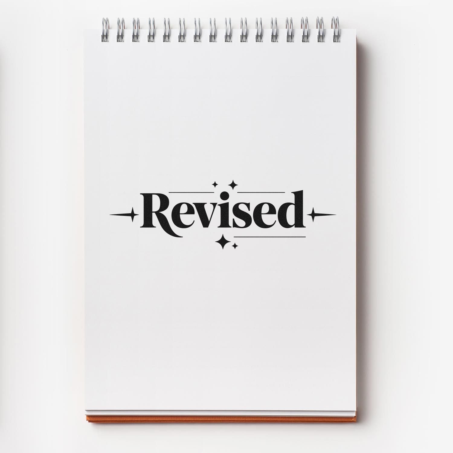 Black Revised stamp and seal on a white spiral notebook with silver rings and tan base.