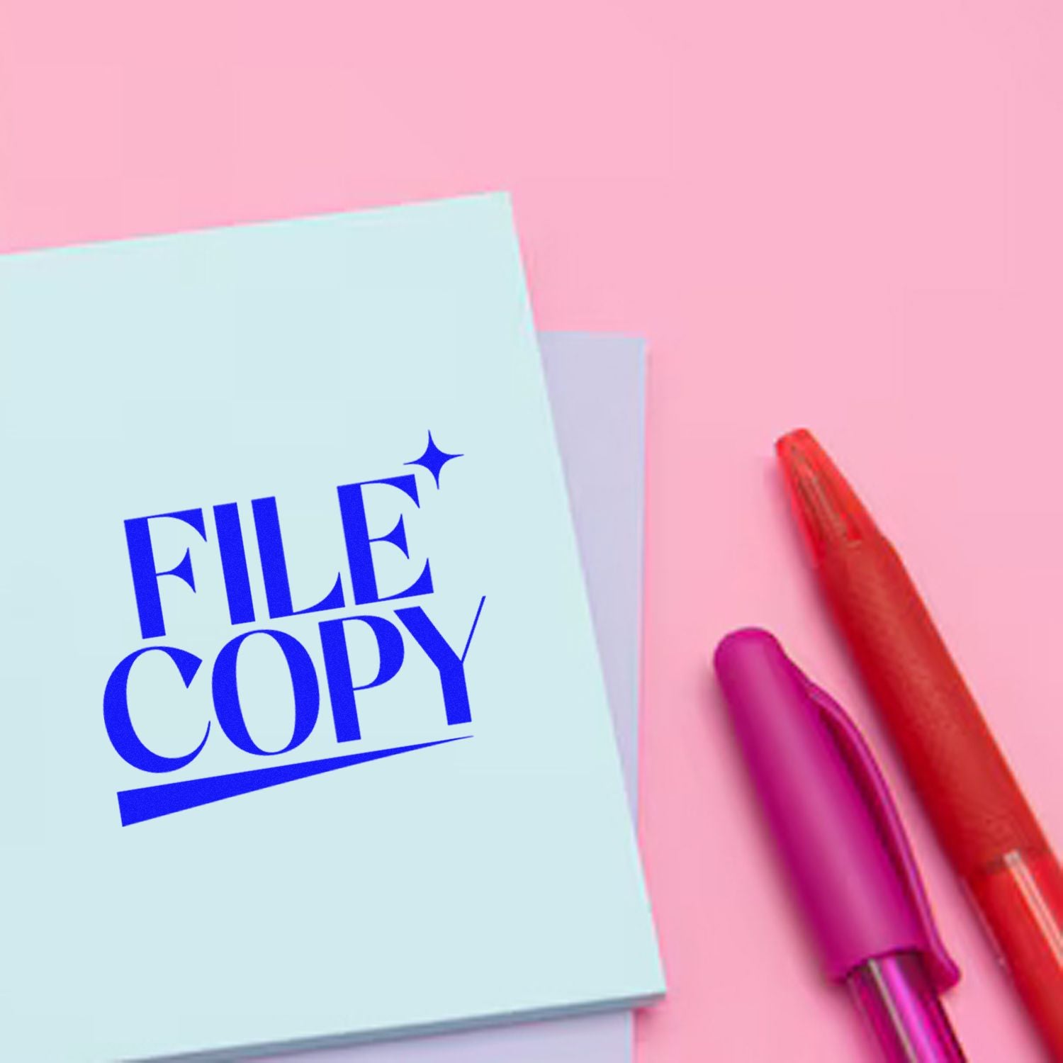 Light blue FILE COPY stamp on pink background with red and magenta pens, showing office stamp and seal products.