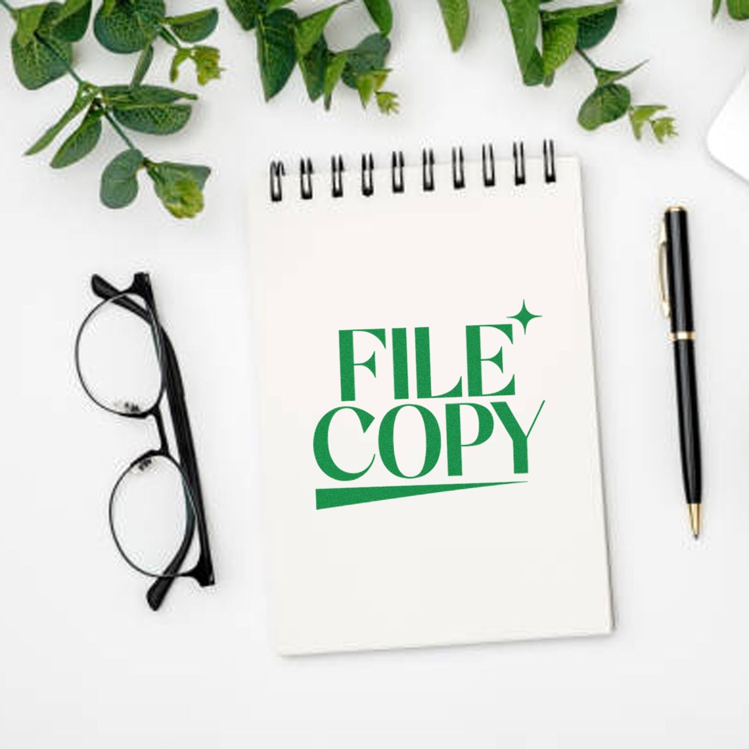 Green FILE COPY stamp seal on a white spiral notebook, with black pen, eyeglasses, and greenery.