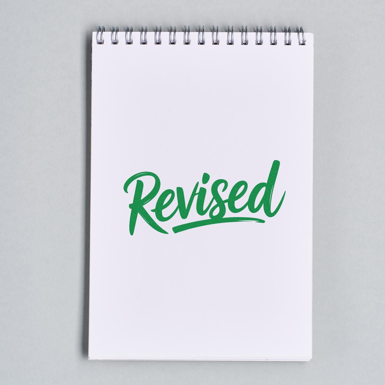 Green Revised stamp seal on a white spiral notepad
