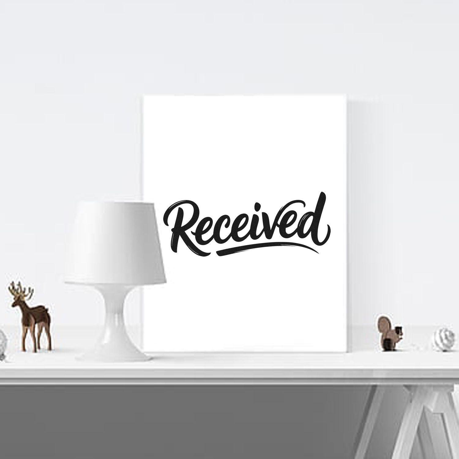 Black Received stamp seal on a white card, with minimalist decor, a white lamp, and small deer figurines.