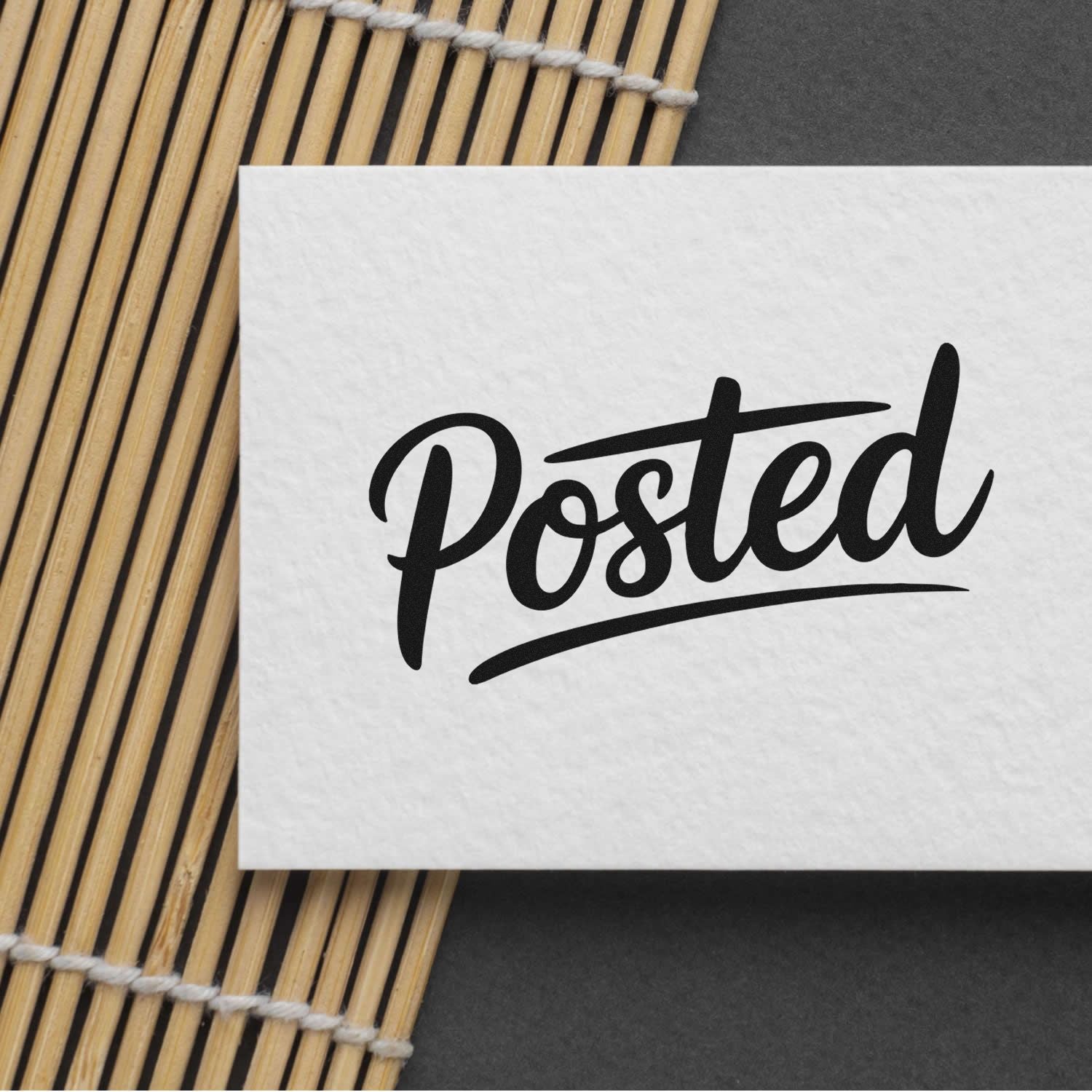White paper card with black Posted stamp seal on a bamboo mat over a dark gray background.