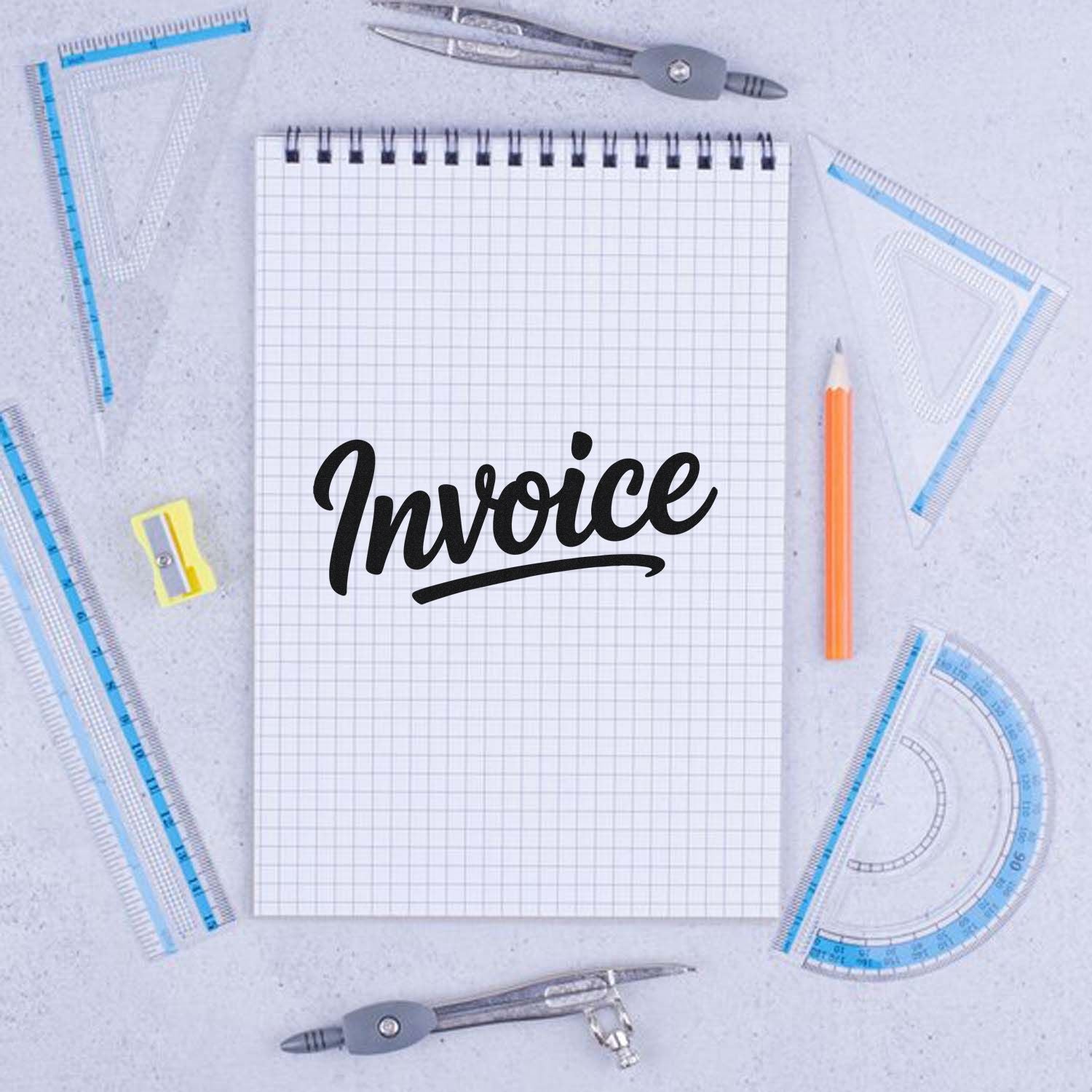 Black invoice stamp on graph notebook, framed by blue drafting rulers, compass, orange pencil, and sharpener.